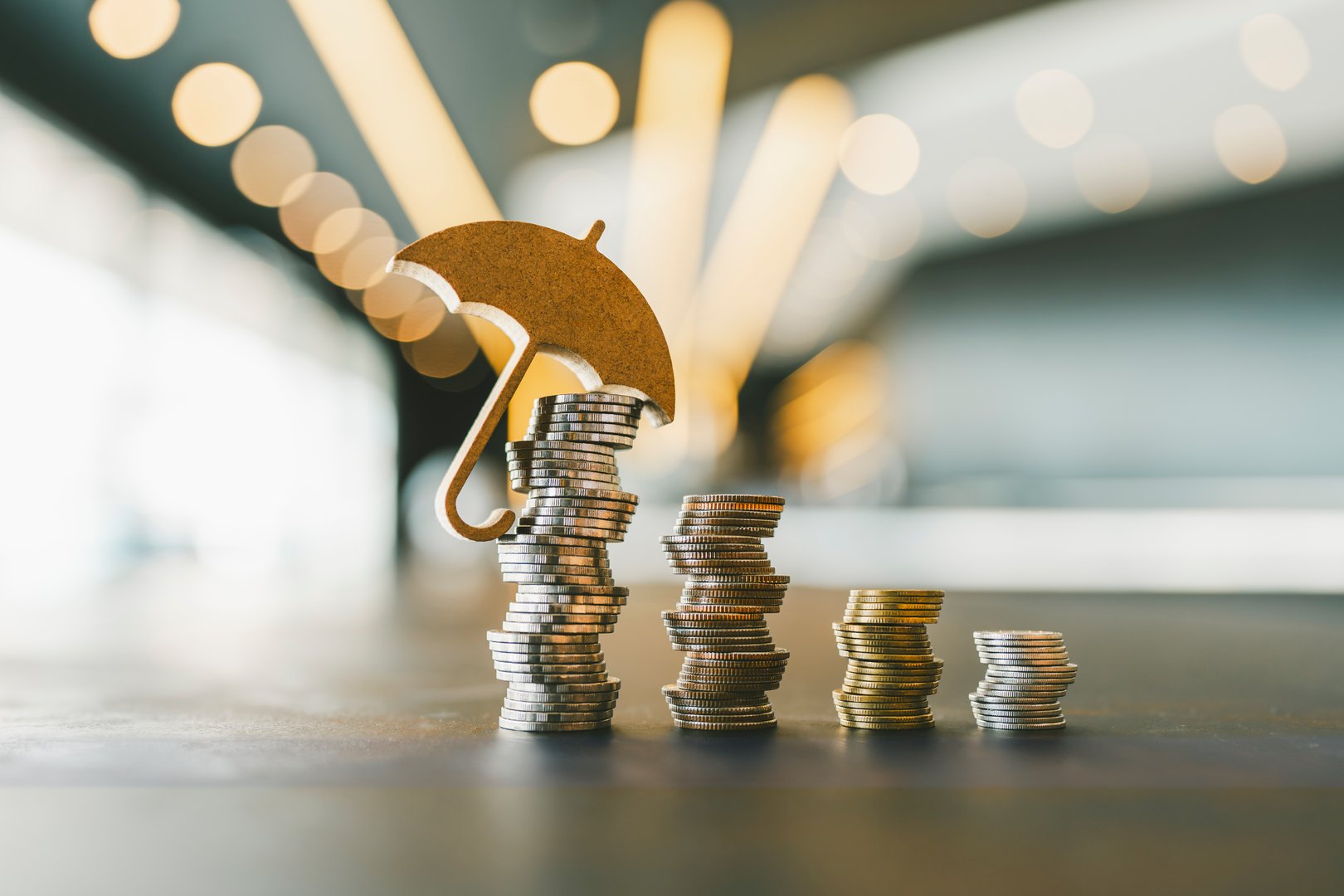 Model umbrella on a pile of money placed on the table is a figure with concepts of deposit guarantee, deposit and wealth maintenance, accumulation insurance.