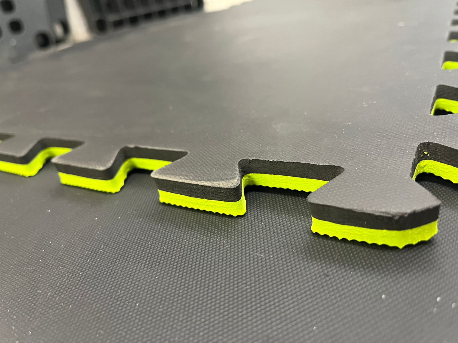 Close-up of interlocking foam mats with black and neon green layers, showing textured edges and a textured surface.