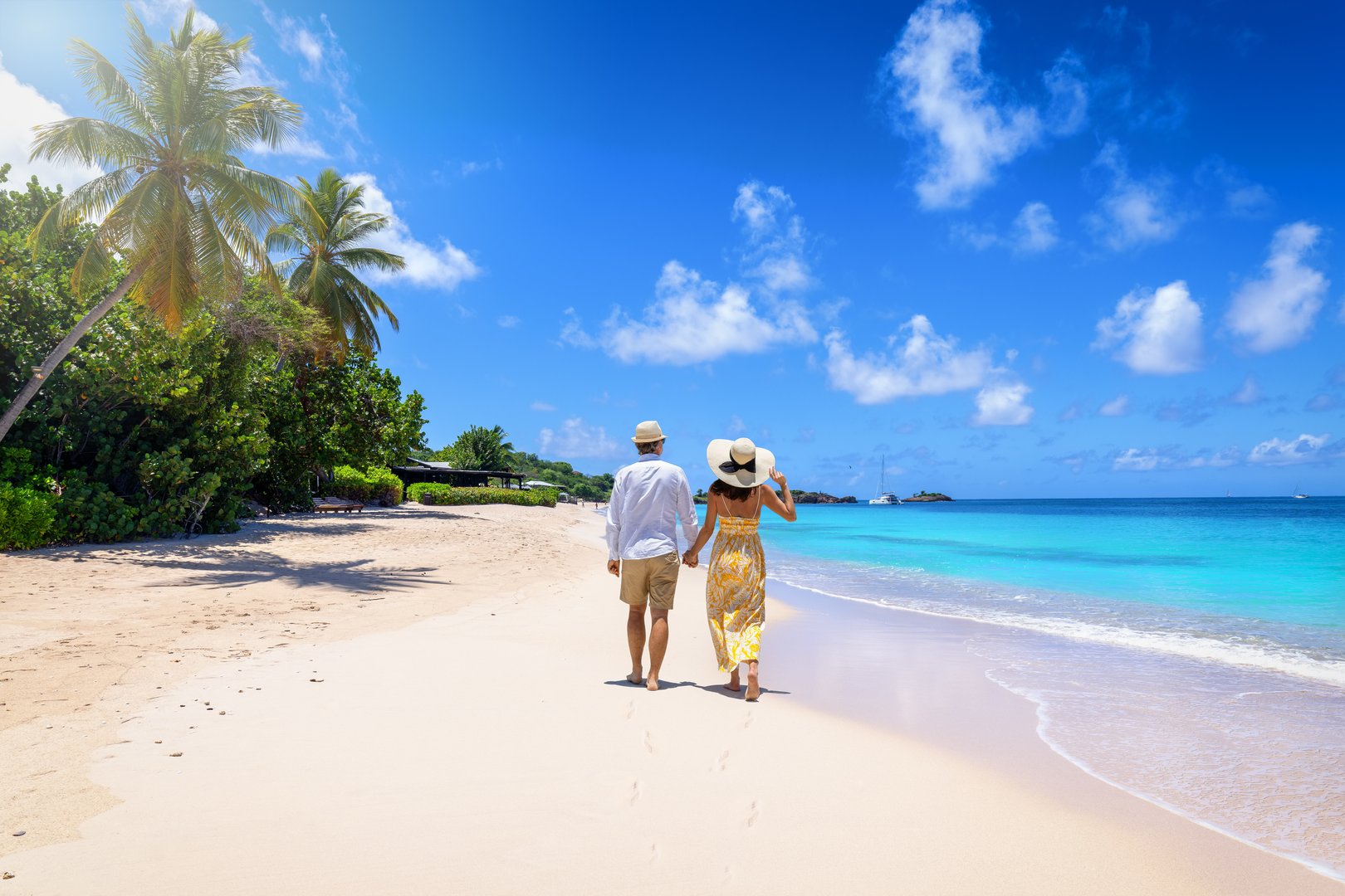 A holiday couple with sunhats walks down the tropical Turners beach with turquoise sea in the Caribbean, Antigua island