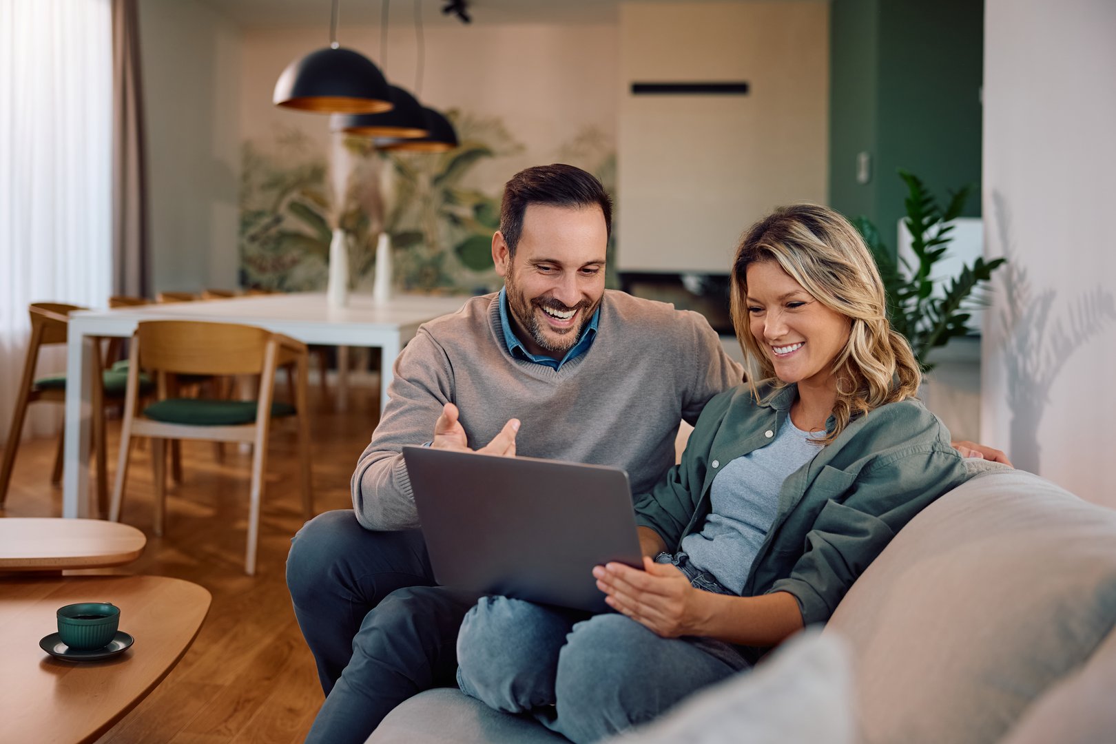 Happy couple using computer while relaxing on the sofa at home.