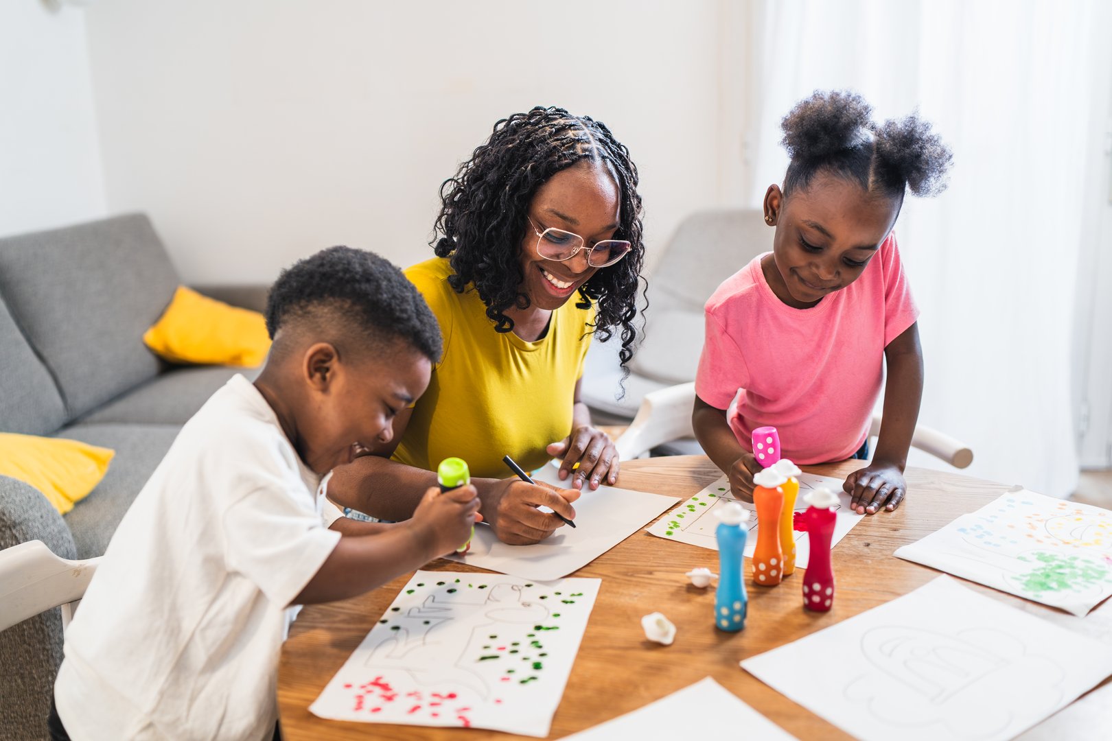 Cheerful african mother assisting her two children while painting and drawing at home, enjoying quality family time