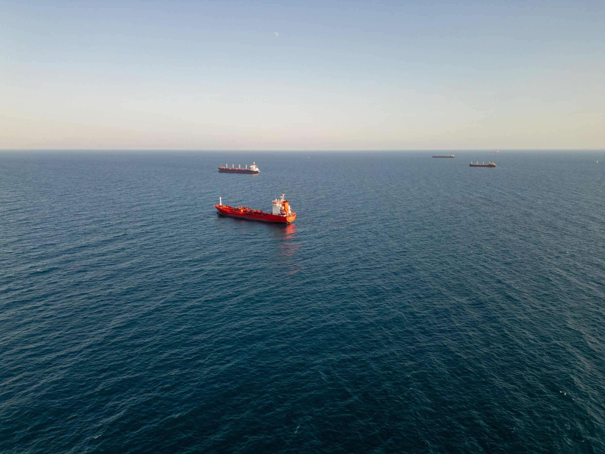 Aerial video of cargo ships anchored in calm open sea under clear sky. Peaceful maritime scene showcasing global trade and ocean transportation at sunrise or sunset.