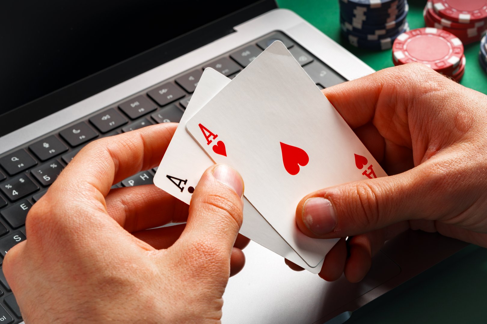 A person is playing online poker. They are sitting at a table with a green felt surface, and they have a laptop in front of them.