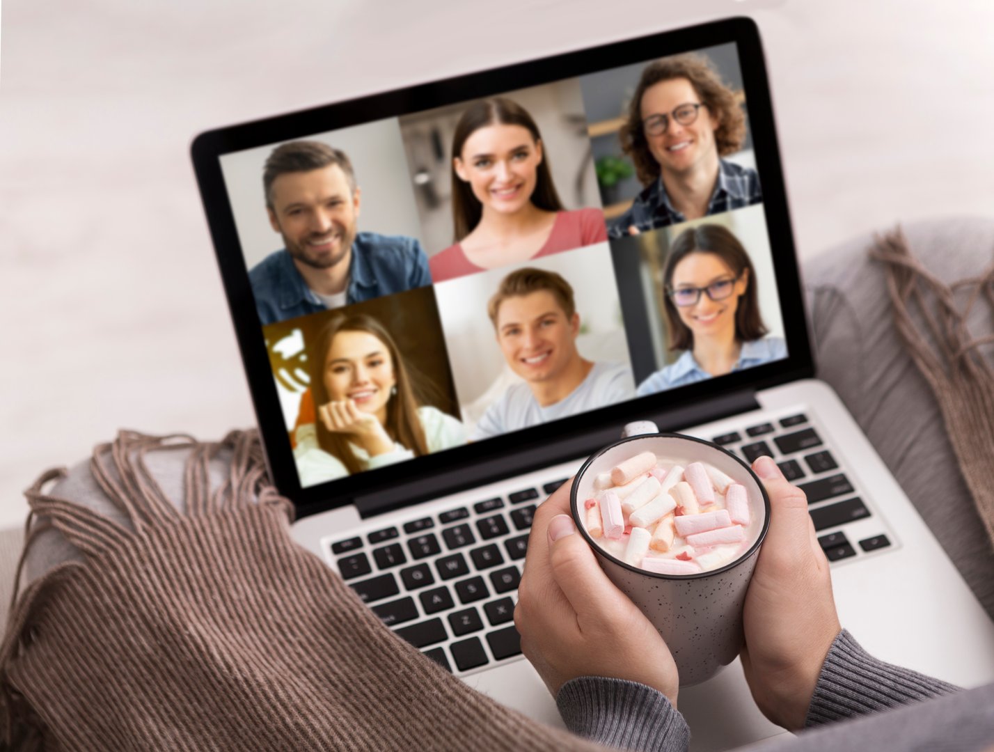 Family online conference during covid-19 pandemic. Social distance and new rules of communication. Young woman with cup of hot cocoa talk with friends on laptop screen, sits on couch with blanket