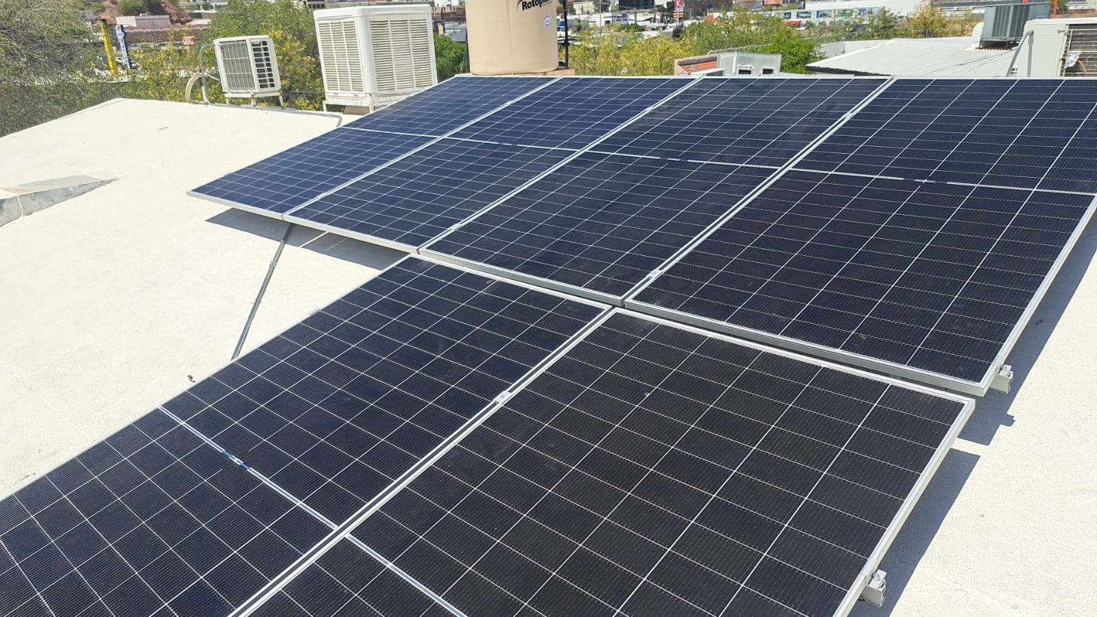 Solar panels installed on a flat rooftop with cityscape and greenery in the background.