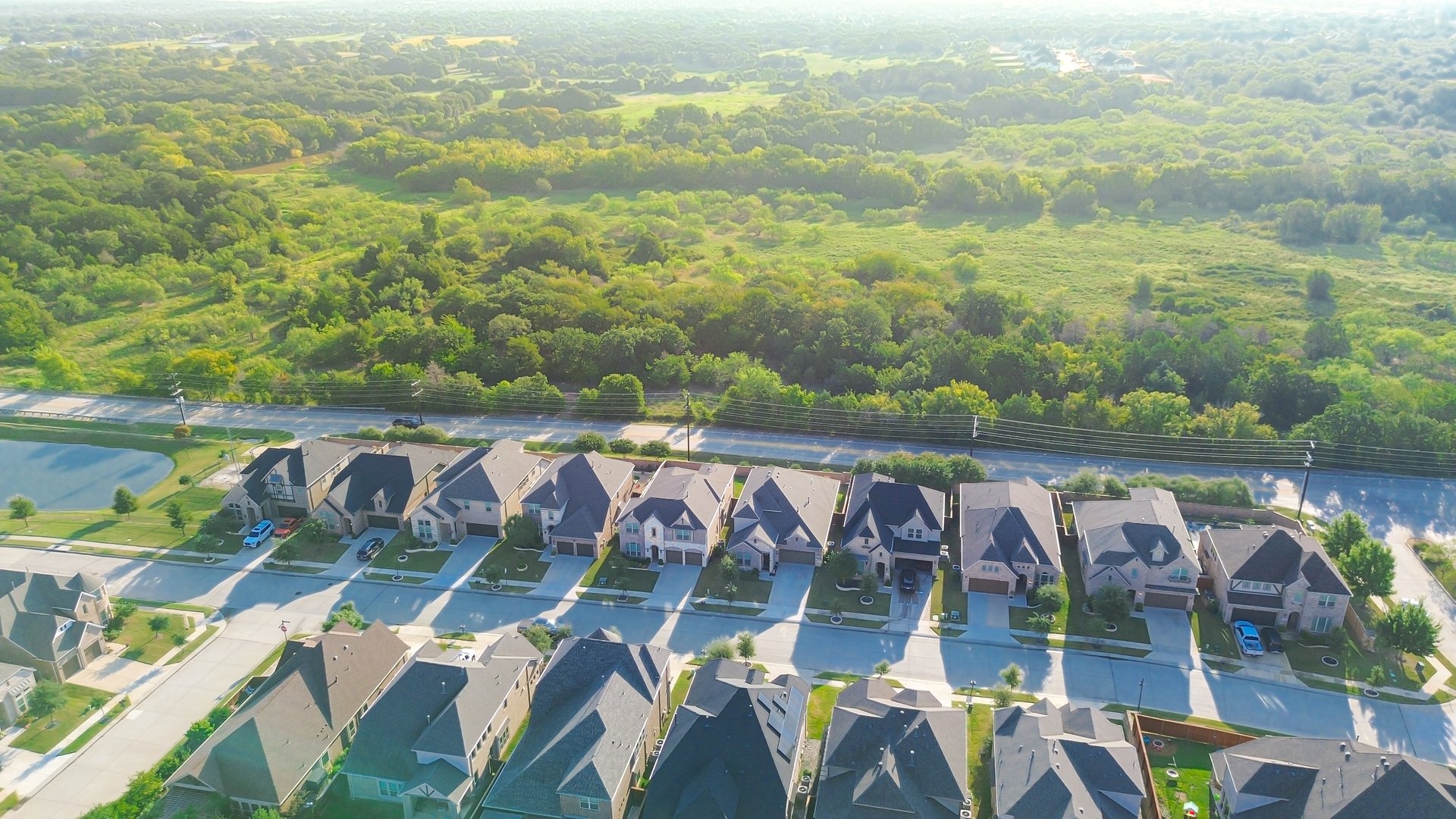Local highway FM 407 separates new development suburban homes with pond in Lantana, Texas from lush greenbelt. Highlights transitional zoning and edge development in master-planned communities. USA