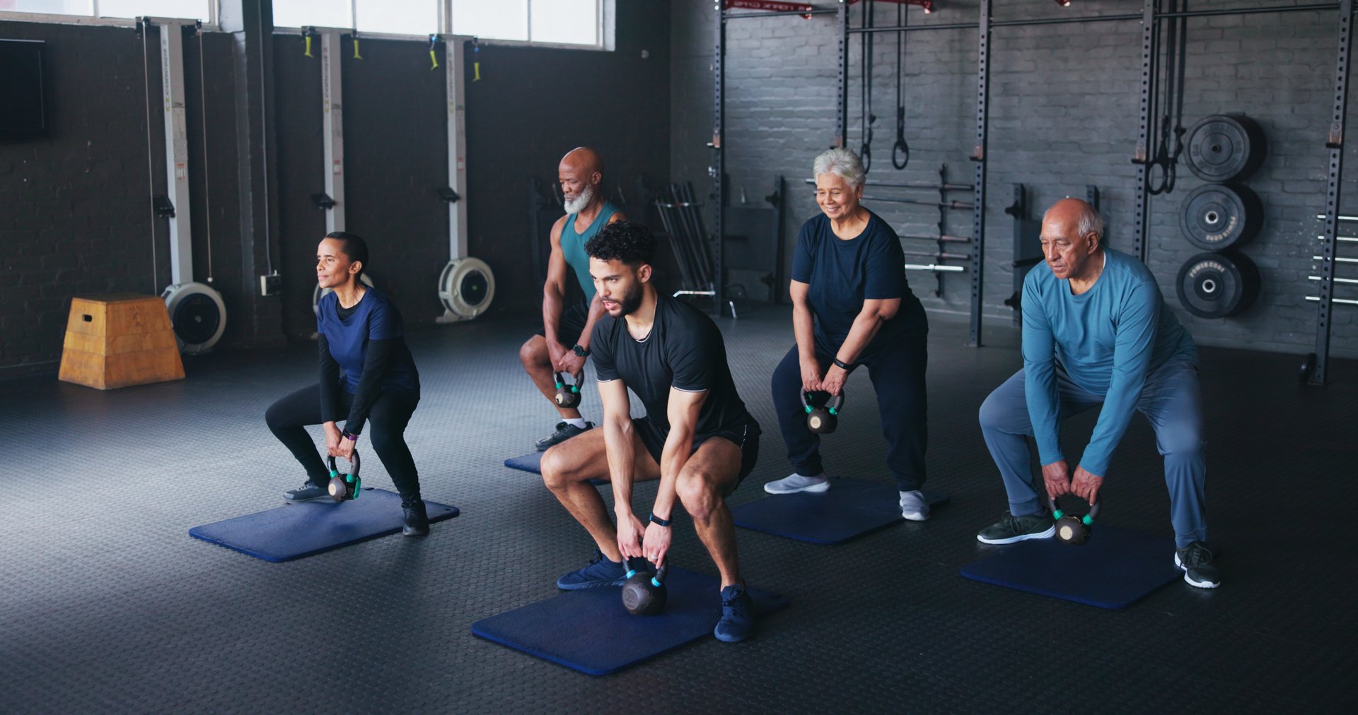 Fitness, kettlebells and people in gym, instructor and training with wellness, weightlifting and exercise. Health club, trainer and senior group with equipment, strength and strong arms with workout