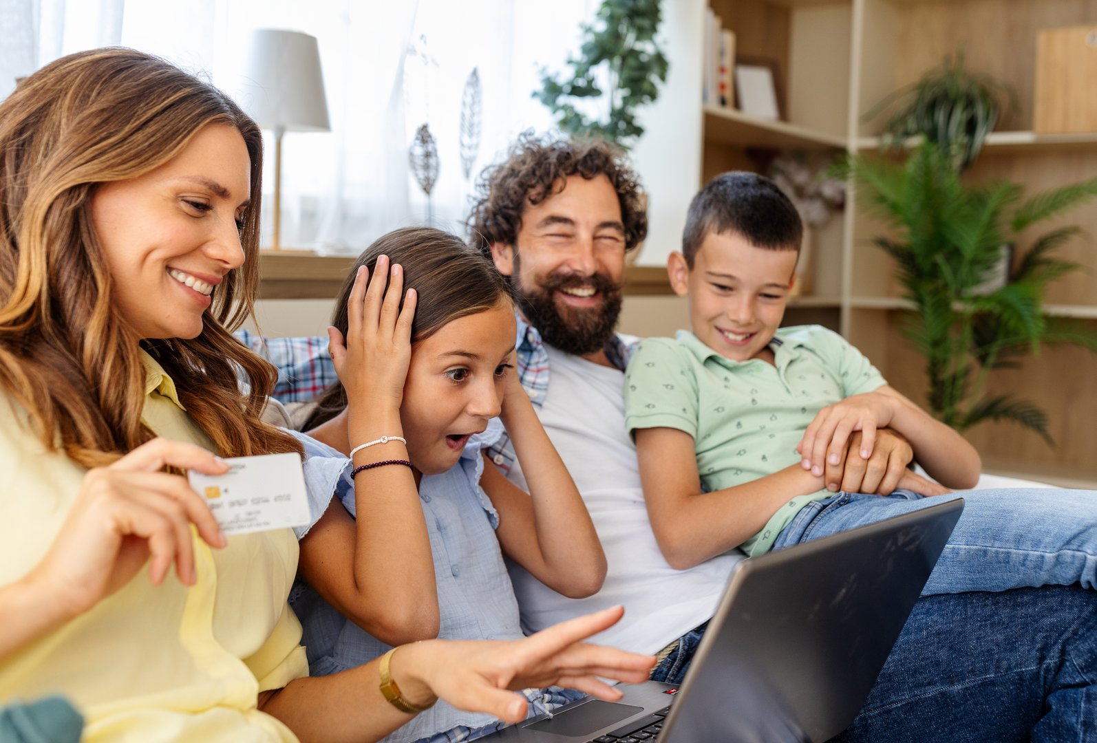 Family is gathered on couch, excited while looking at laptop. The children show astonishment, sharing joyful moment together