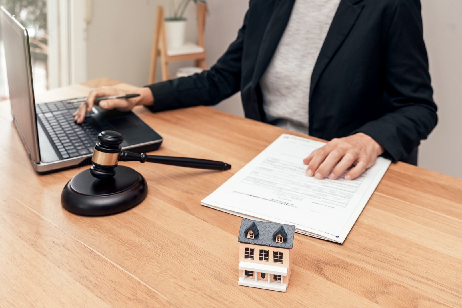 Lawyer working on a laptop with a gavel and a miniature house model on a wooden desk, discussing mortgage or insurance contract