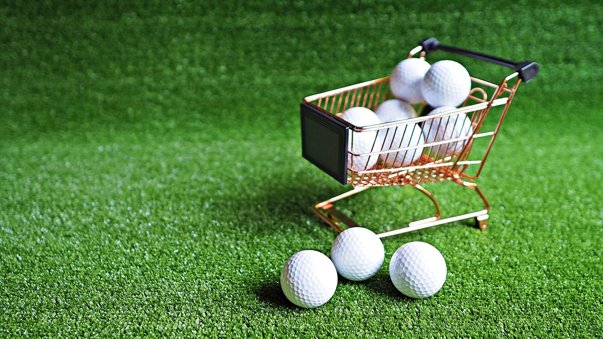 Close up on golf balls on brass shopping trolley with green grass background. Golf sport background.