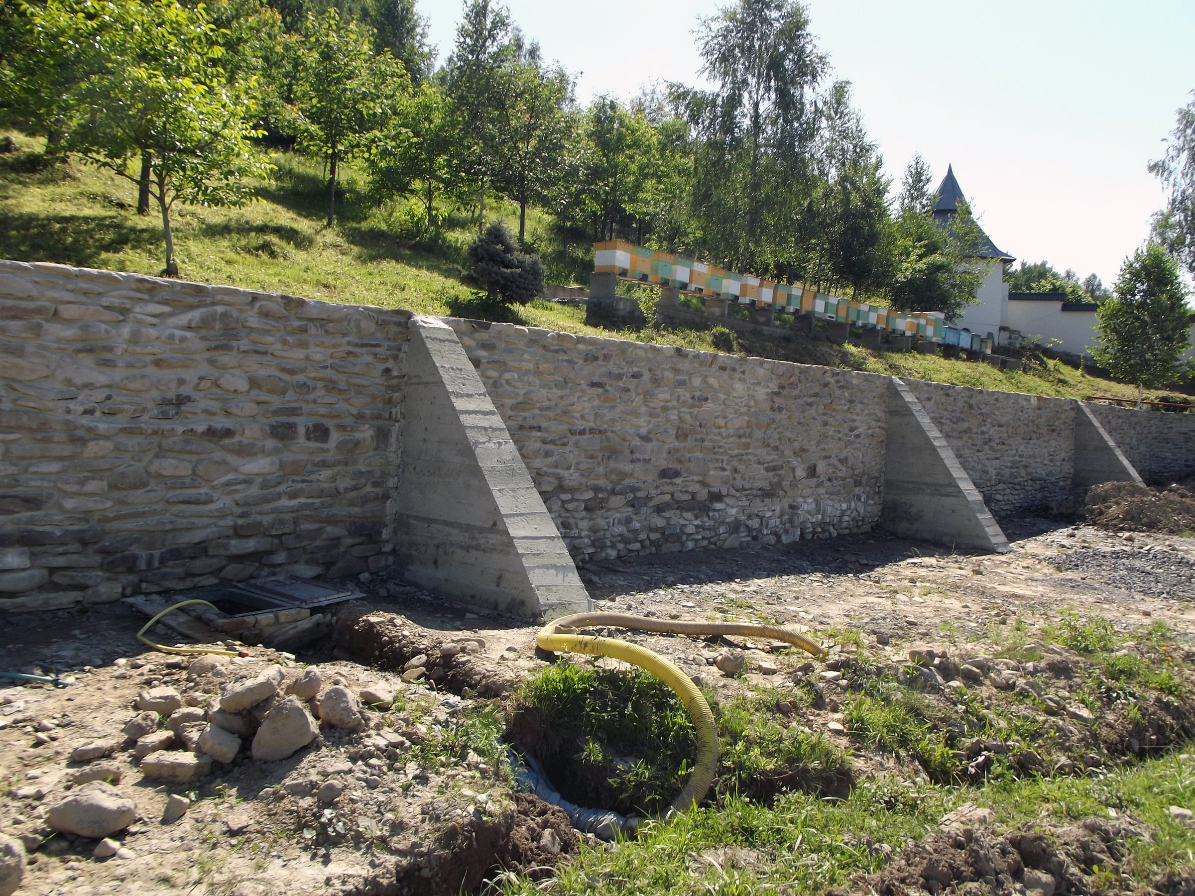 Segmented stone retaining wall with concrete support beams integrated into sloped landscaped terrain in private garden development project
