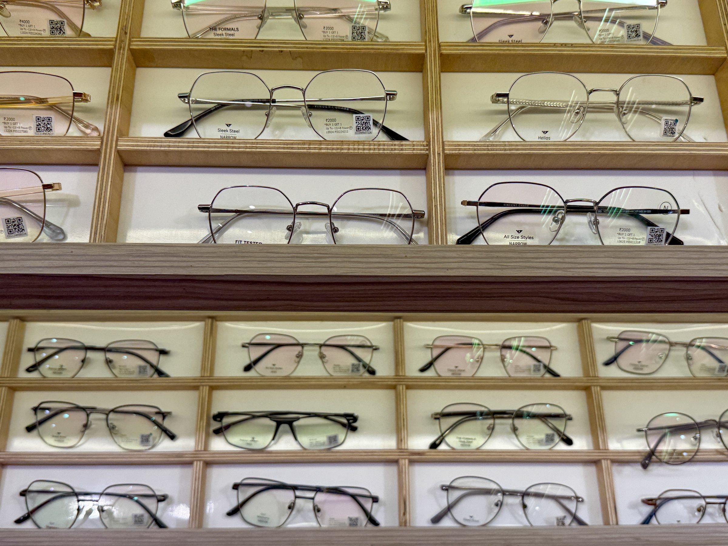 A display of eyeglasses with a variety of styles and colors. The glasses are arranged in a wooden case, with some of them being on the top shelf and others on the bottom. The display is organized