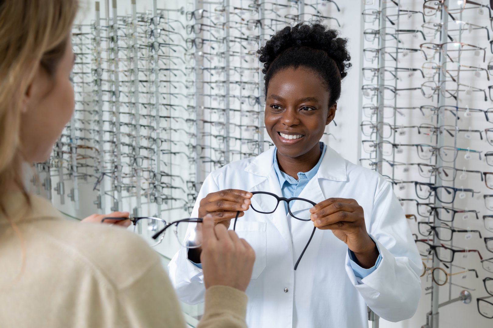 In optic shop. Smiling optician presenting new eyeglasses to a blonde female client