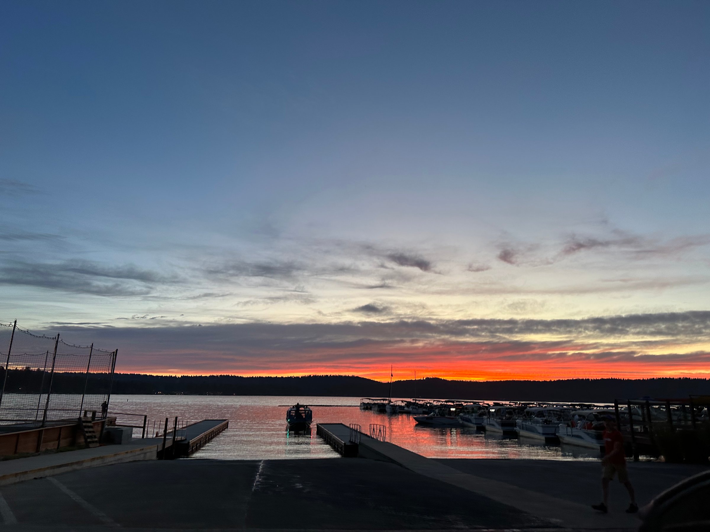 Dusk scene of a marina with boats docked, silhouetted against a vivid orange and purple sunset sky.