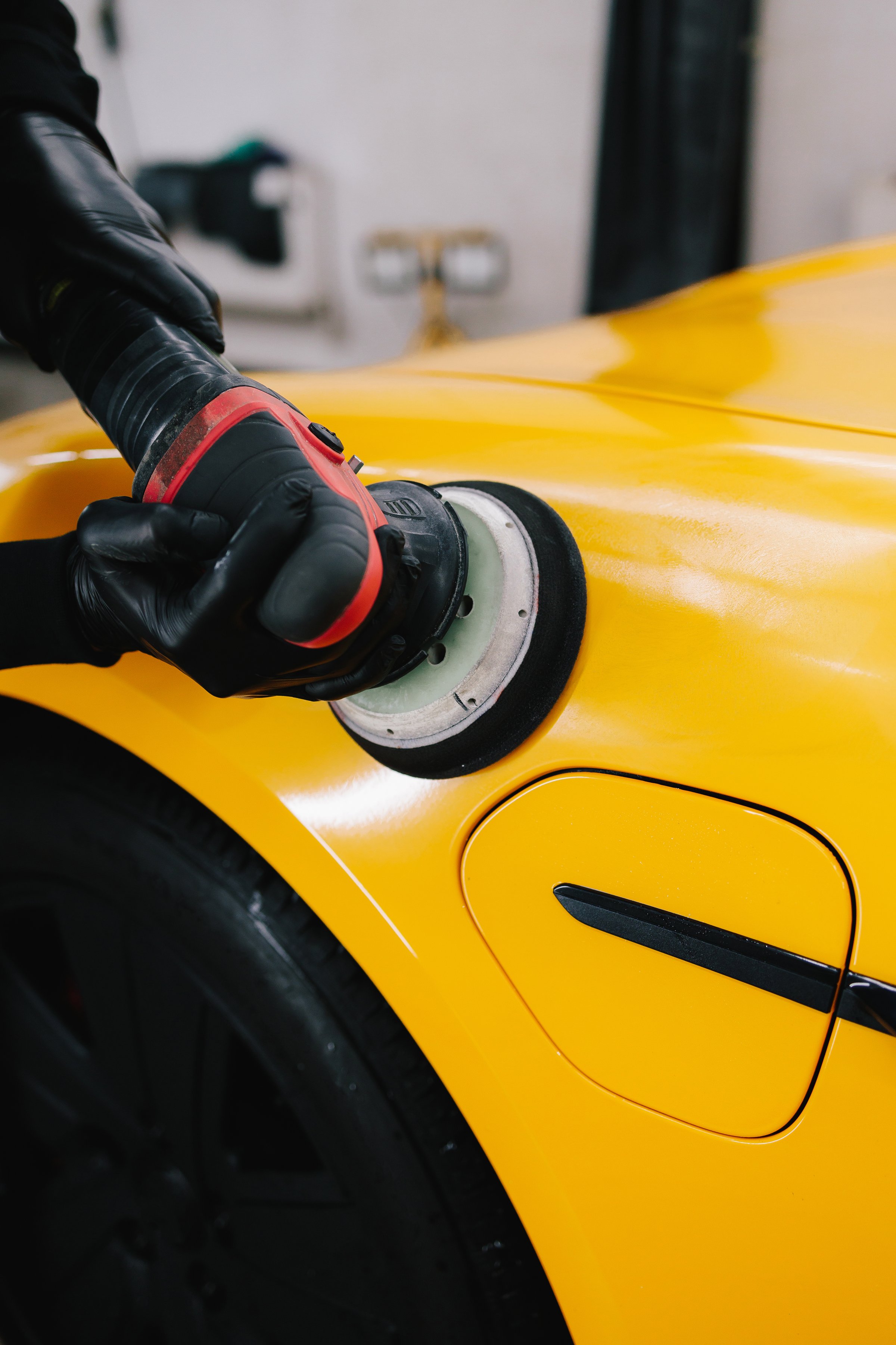 Polishing sports car using abrasive paste with orbital polisher for remove scratches. Hands of car service worker with orbital polisher polishing car hood in repair shop