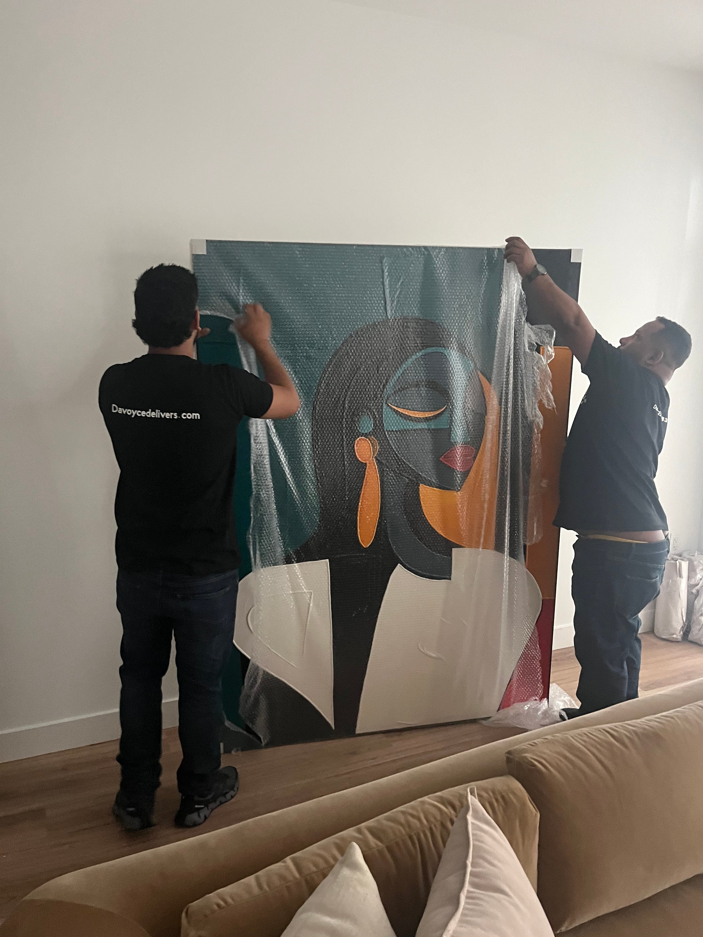 Two men unwrapping a large, colorful abstract portrait painting in a living room.