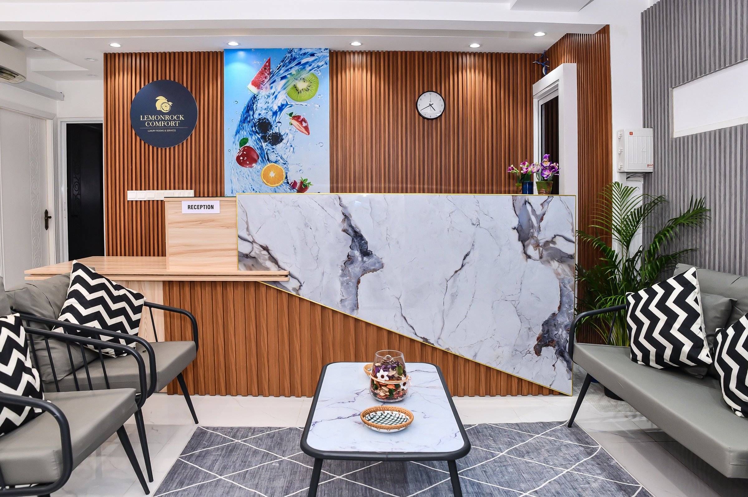 Modern reception area with marble counter, wood paneling, wall art, and seating. Zigzag pillows and geometric decor accents.