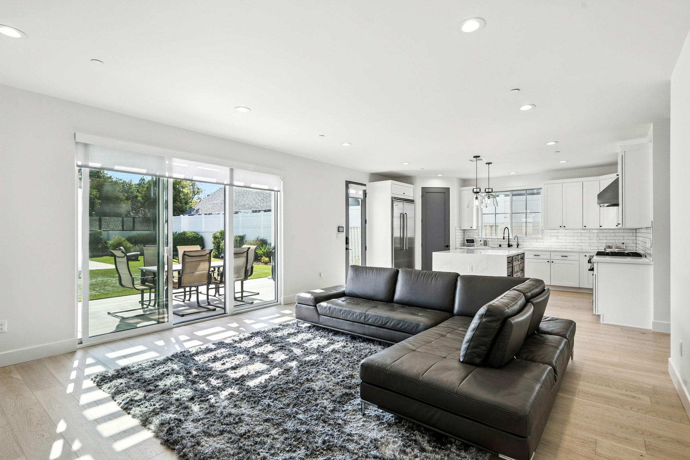 Modern open-plan living room with dark leather sofa, kitchen, and patio view through sliding glass doors
