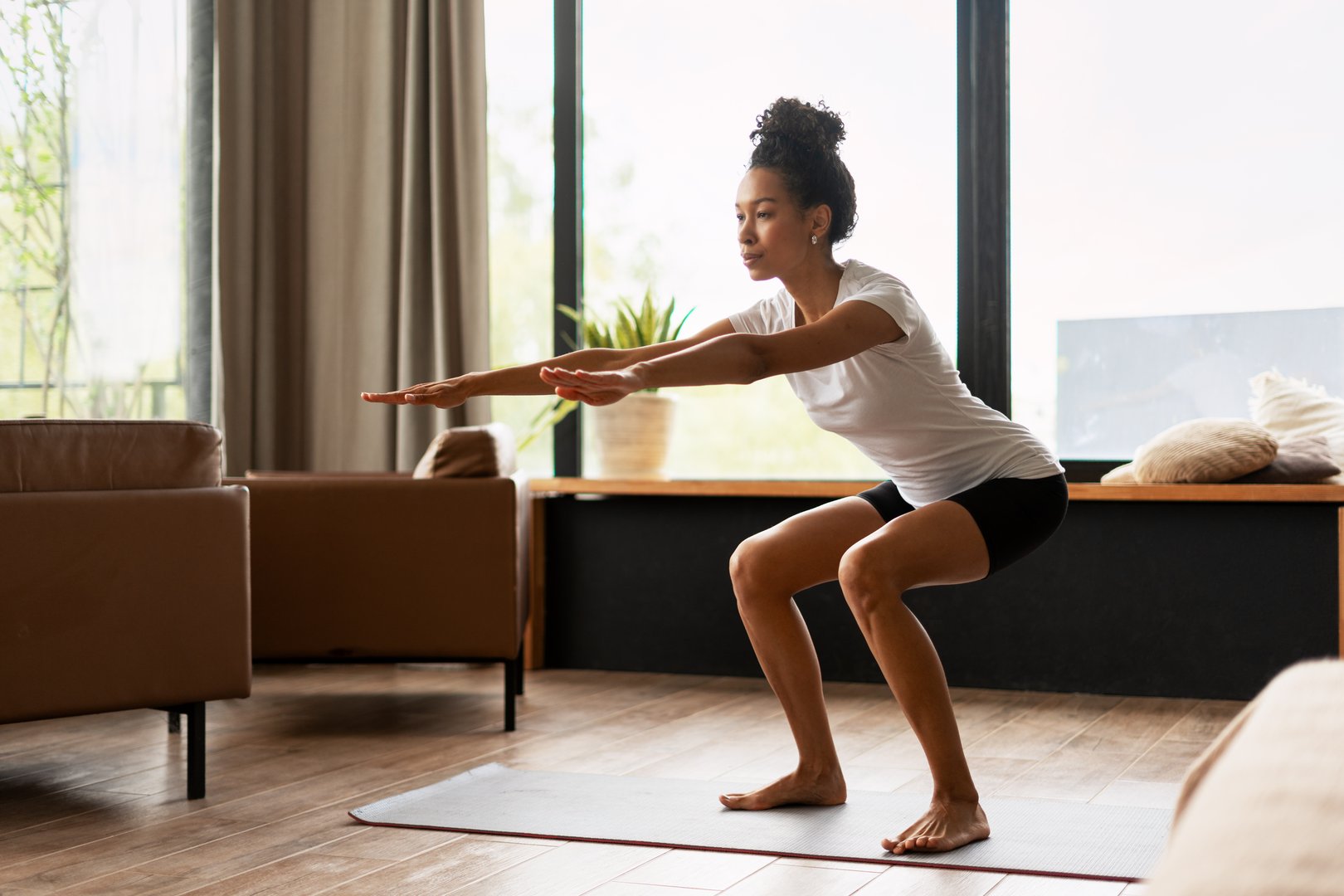 Young woman exercising at home, performing squats on a yoga mat in her cozy living room, embracing a healthy and active lifestyle