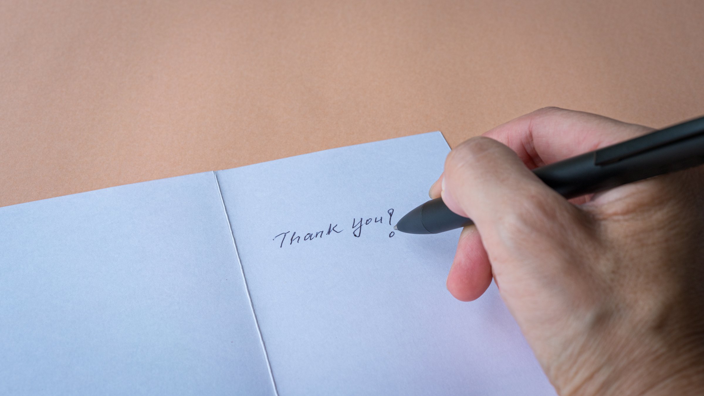 Woman writing on a thank you card, close up view.