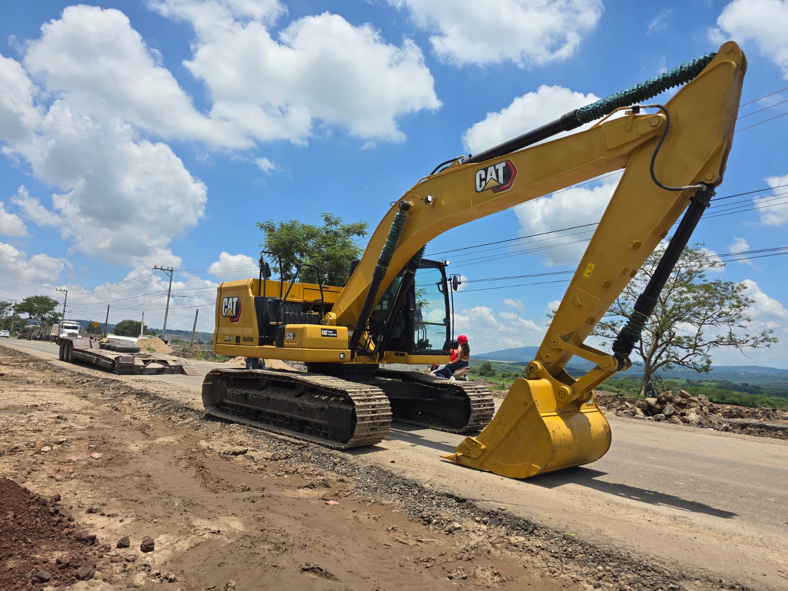 Yellow excavator on a road construction site under a blue sky with white clouds.