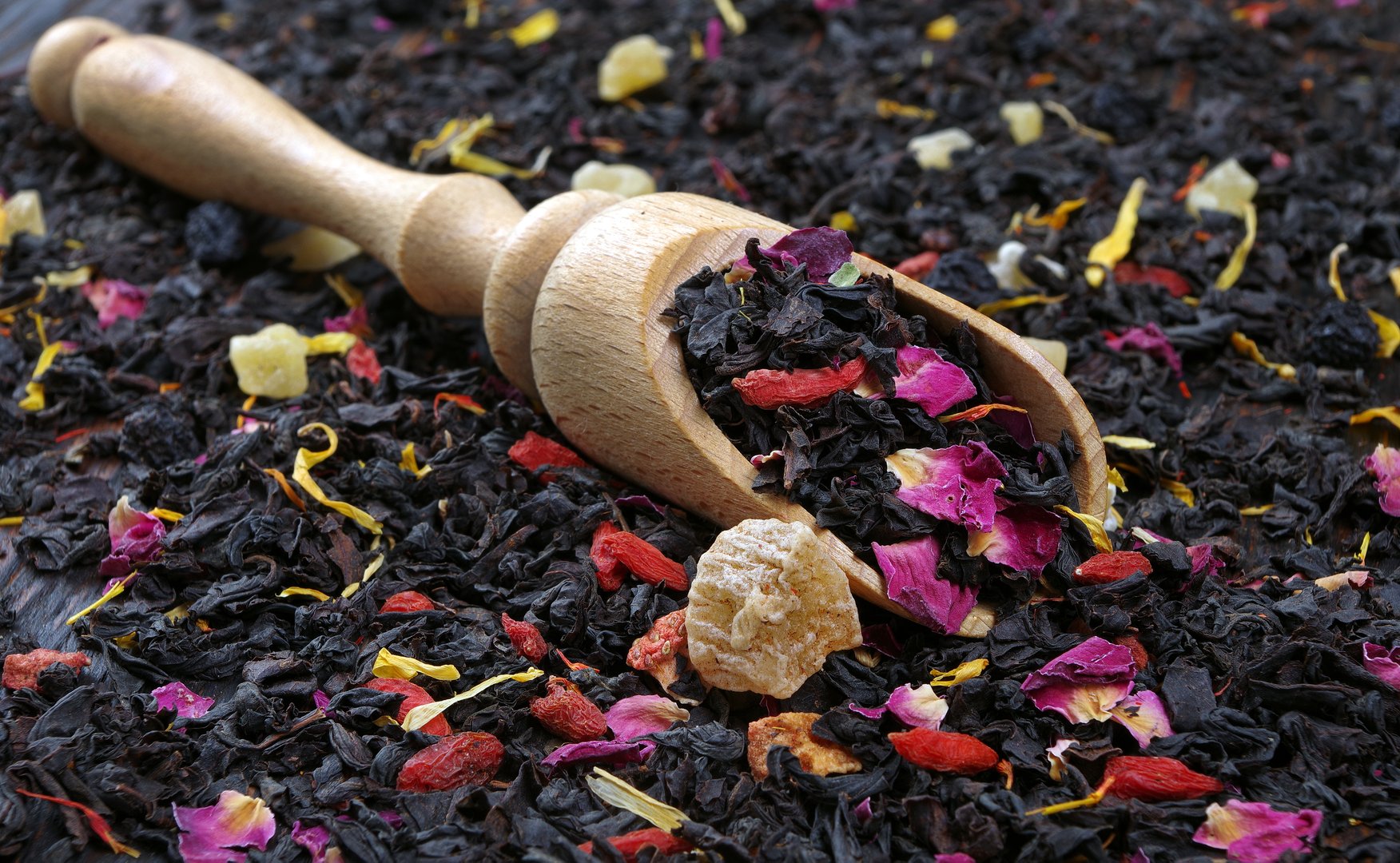 black blended tea with flower petals and dried fruit on a wooden scoop. close up