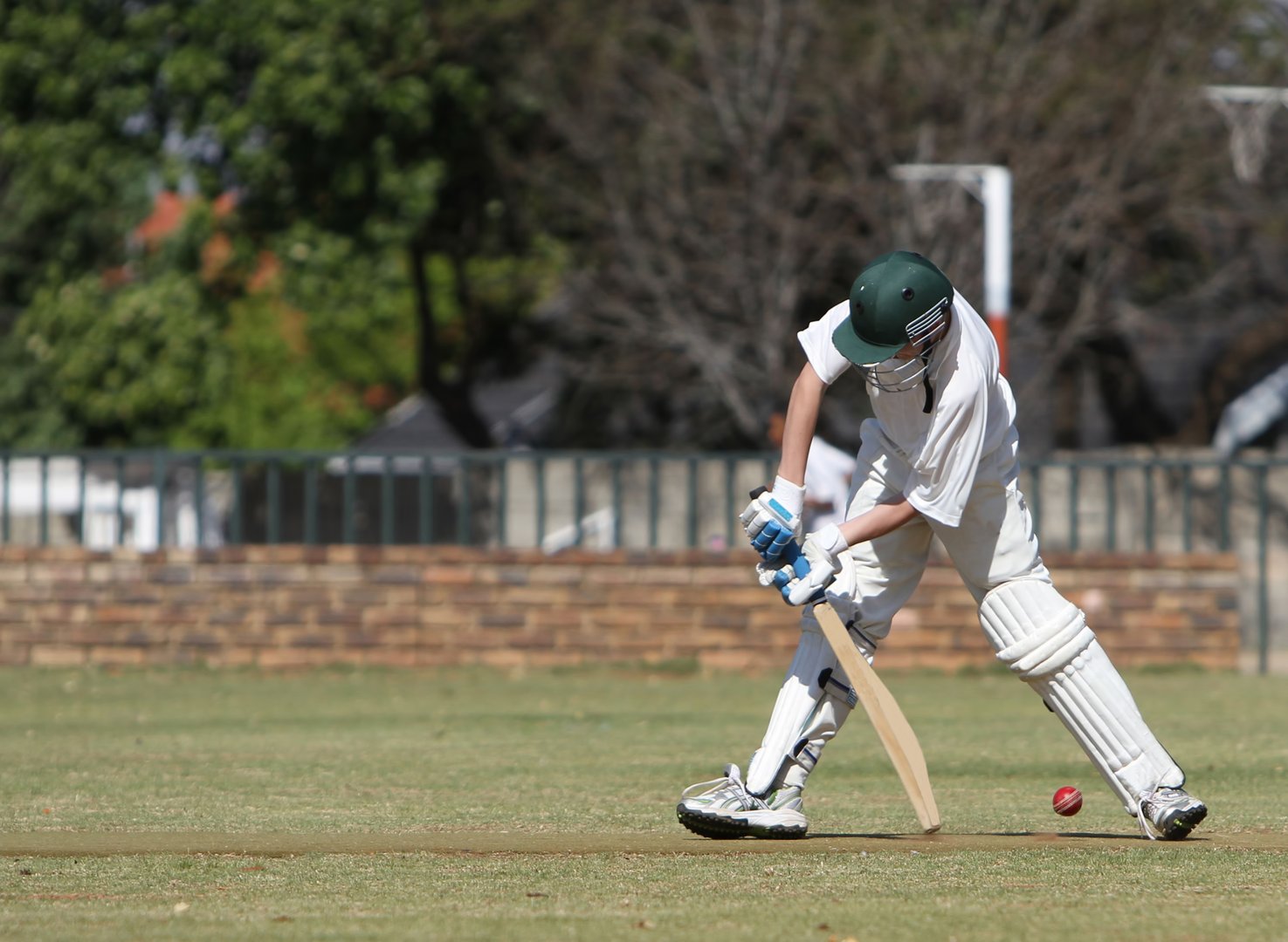 A young left handed cricket batsmen is hitting a cricket ball with his bat. He is fully clothed in white clothing and pads, helmet and gloves.