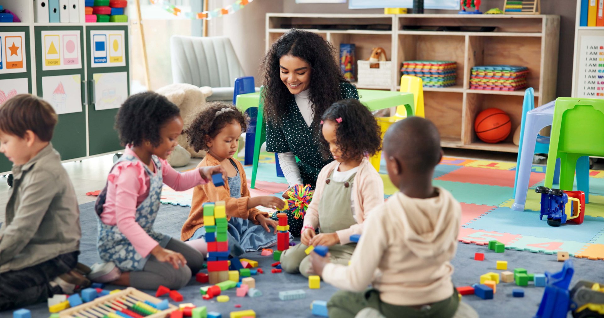 Building blocks, education and teacher with children in classroom for learning, playful or creative games. Growth, kindergarten or academy with woman and kids at school for toys and child development