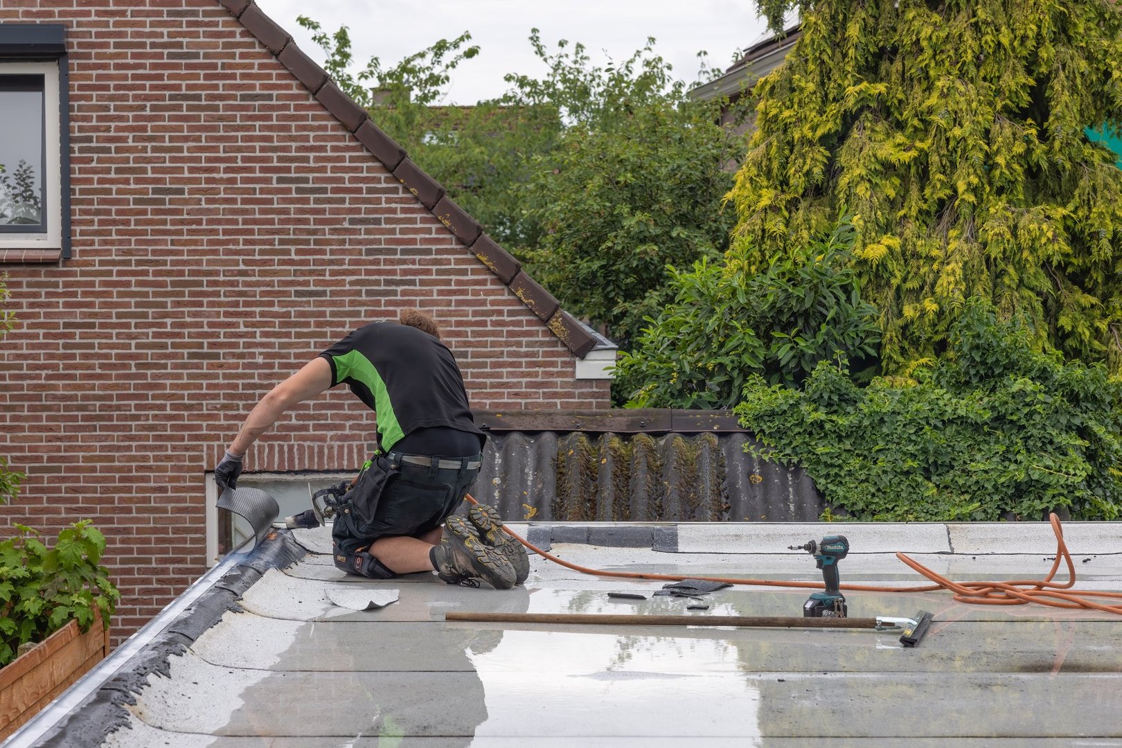 Workers at flat roof preparing rolls of new white roofing felt