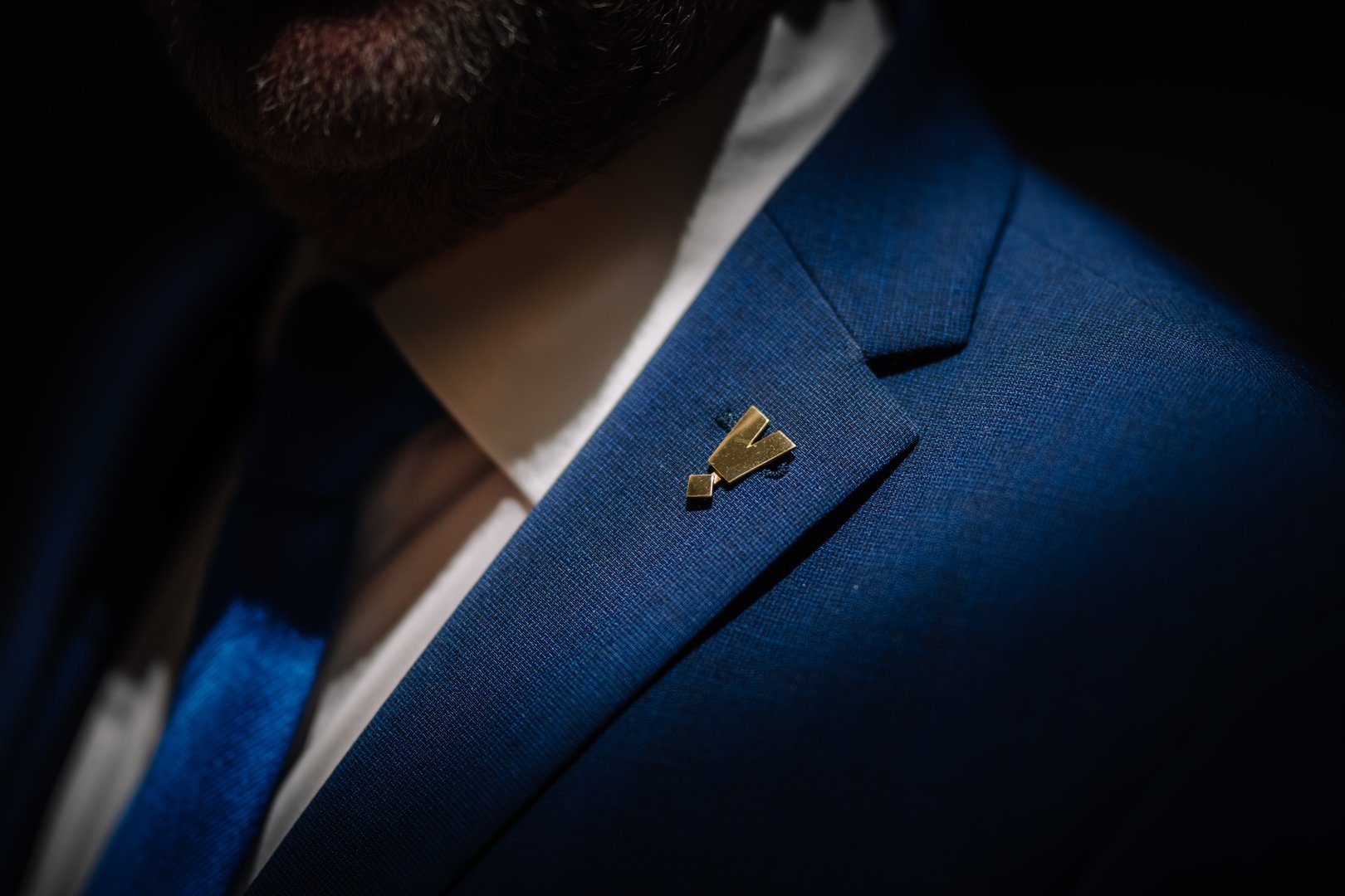 Valmiera, Latvia - October 11, 2024 - Vecpuisis. A close-up of a gold lapel pin on a blue suit jacket, highlighting the texture and details of the fabric under focused light, with a hint of a tie.