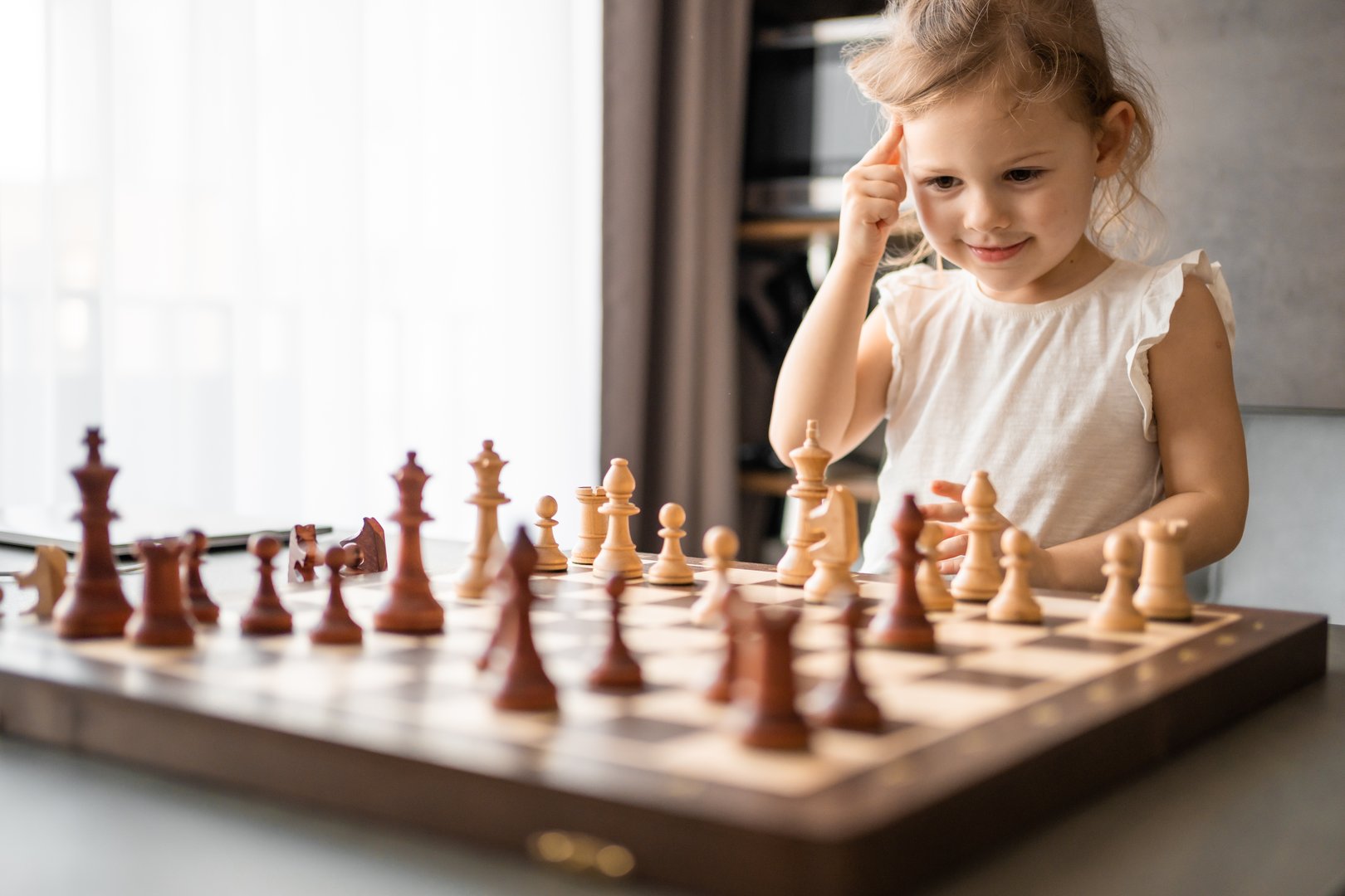 Little girl playing chess at the table in home kitchen. The concept early childhood development and education. Family leisure, communication and recreation. High quality photo