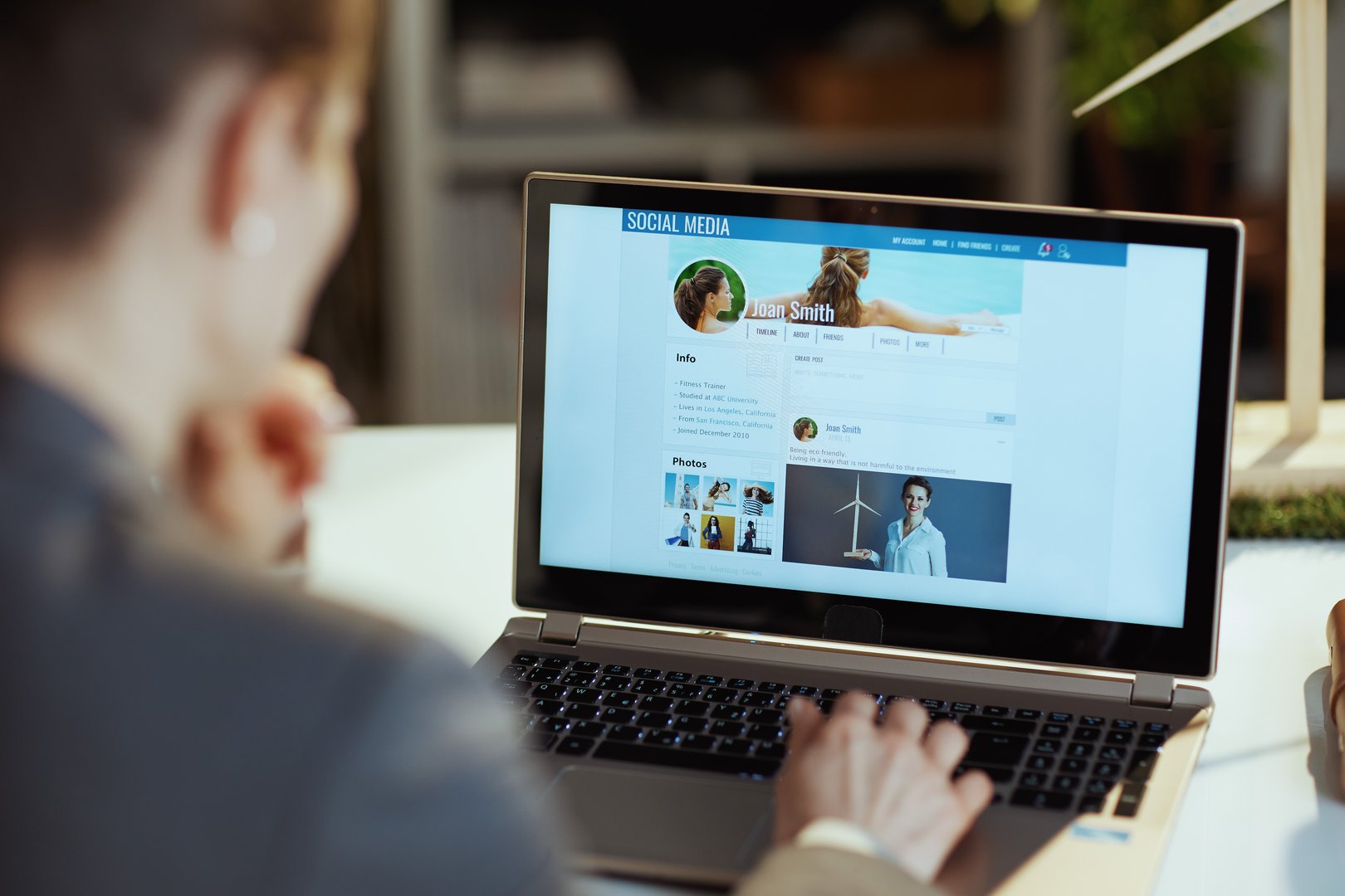Seen from behind modern woman with laptop in modern office reading news on social media.