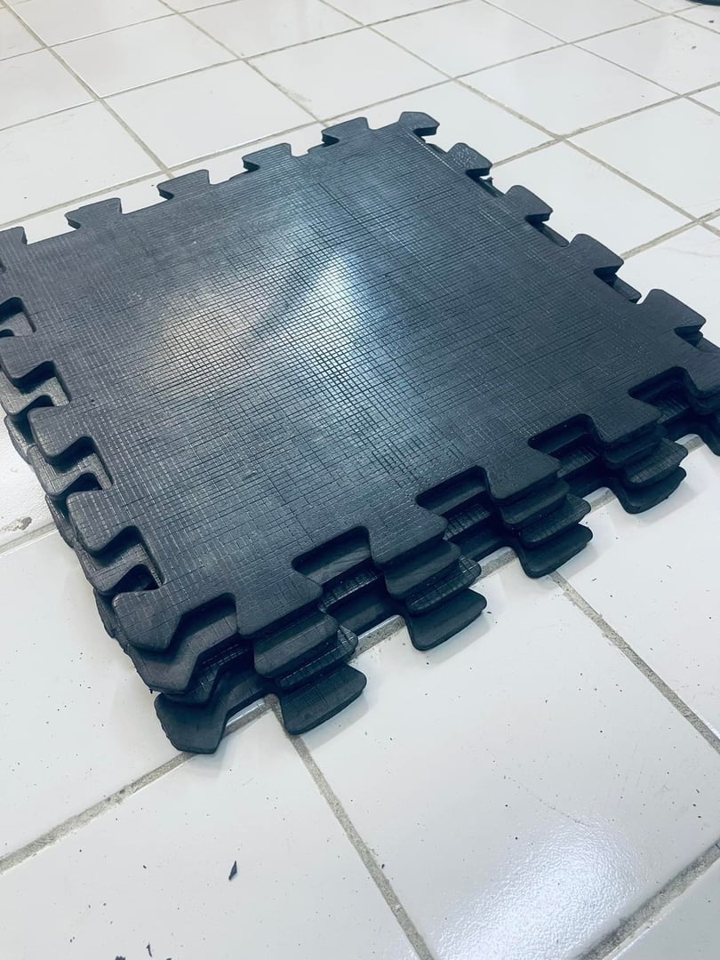 Stack of interlocking black foam floor mats on white tiled floor.