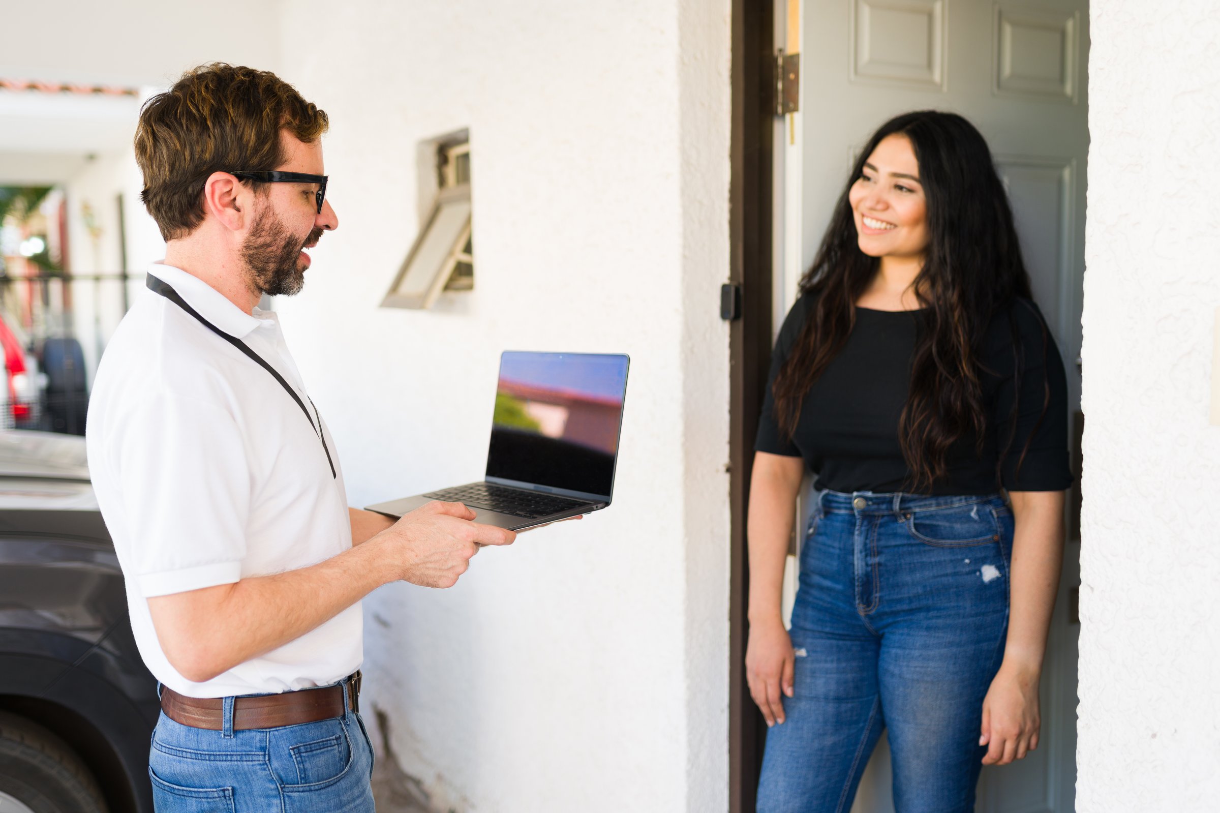 Salesman presenting information on a laptop to a smiling female customer visiting her at home for a door-to-door service