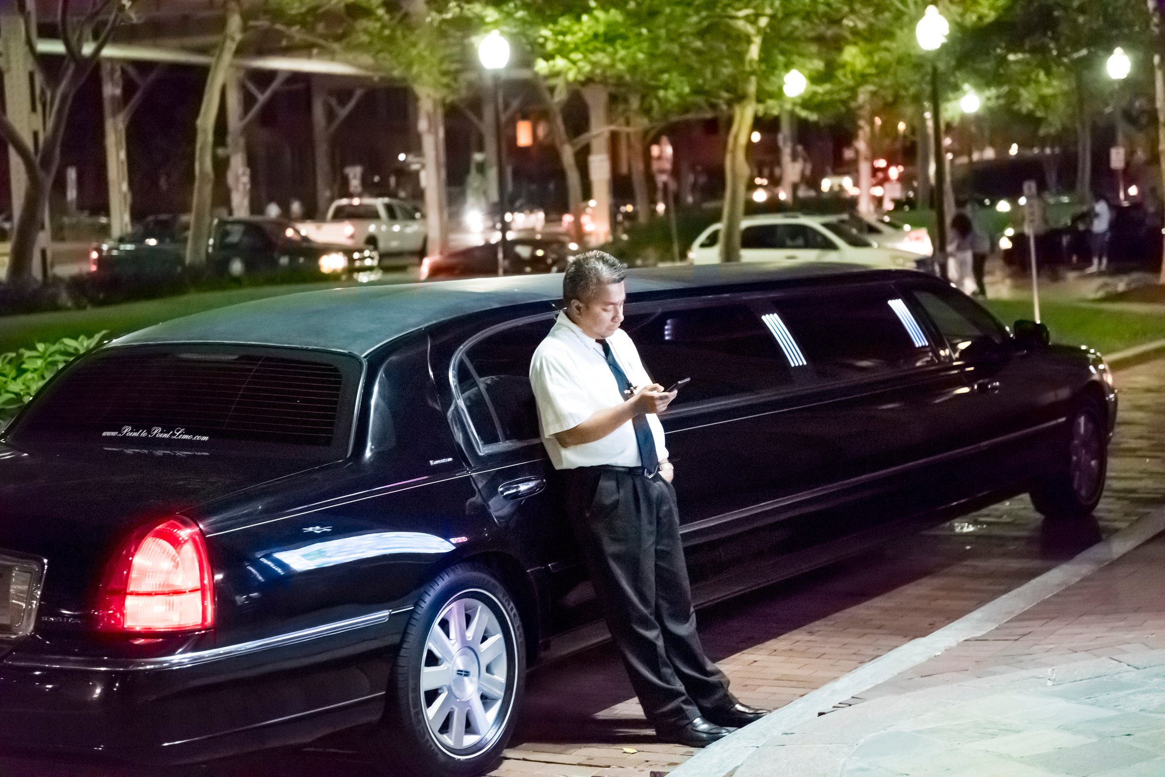 Washington Dc: Limo limousine driver standing by car sidewalk looking at mobile smartphone phone in Georgetown neighborhood during dark night nightlife evening