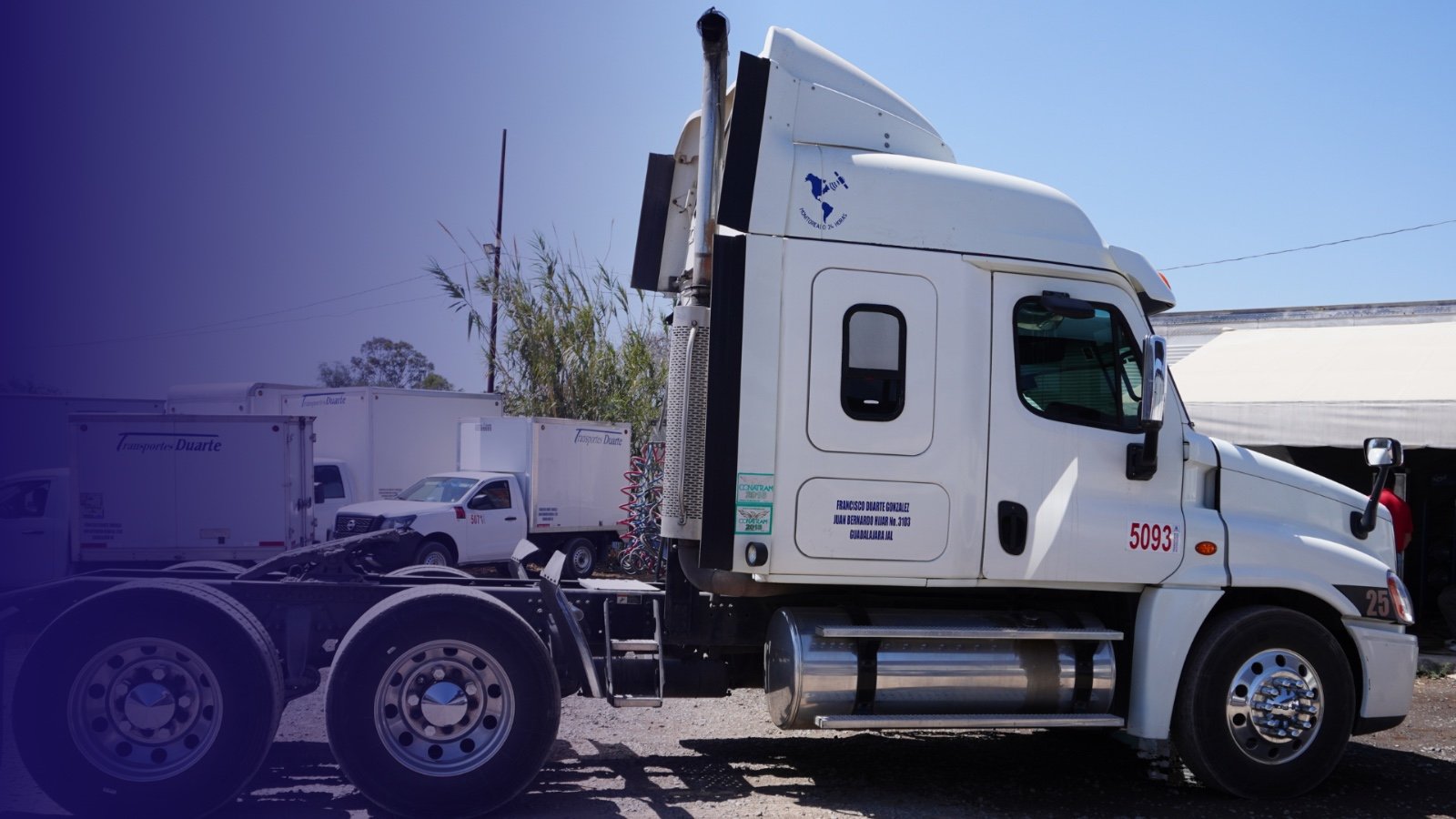 White semi-truck parked in a lot with other trucks, featuring a logo on the cabin and a blue hue on the left edge.