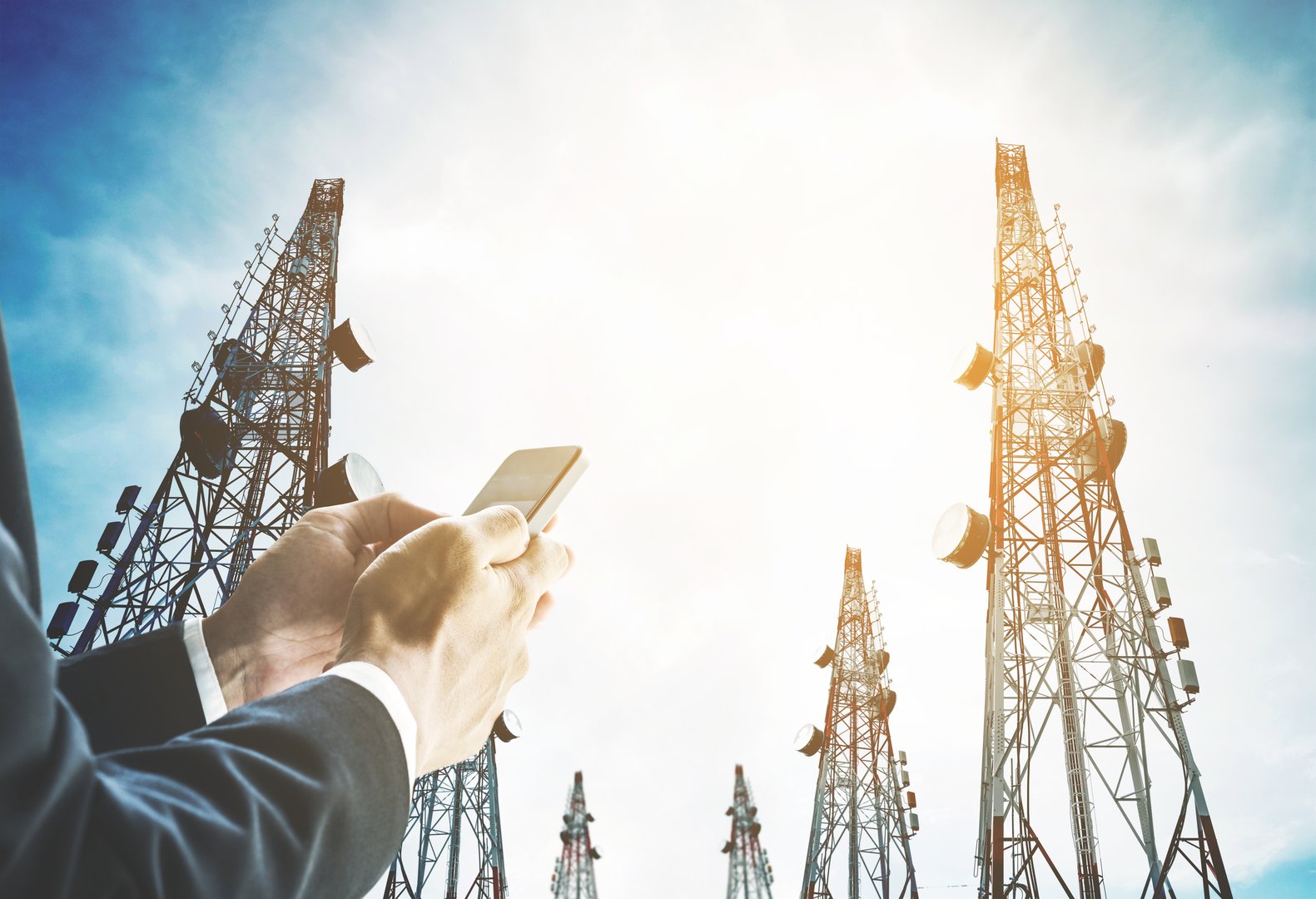 Businessman using mobile phone with Telecommunication towers with TV antennas and satellite dish in sunrise, vintage tone, soft focus