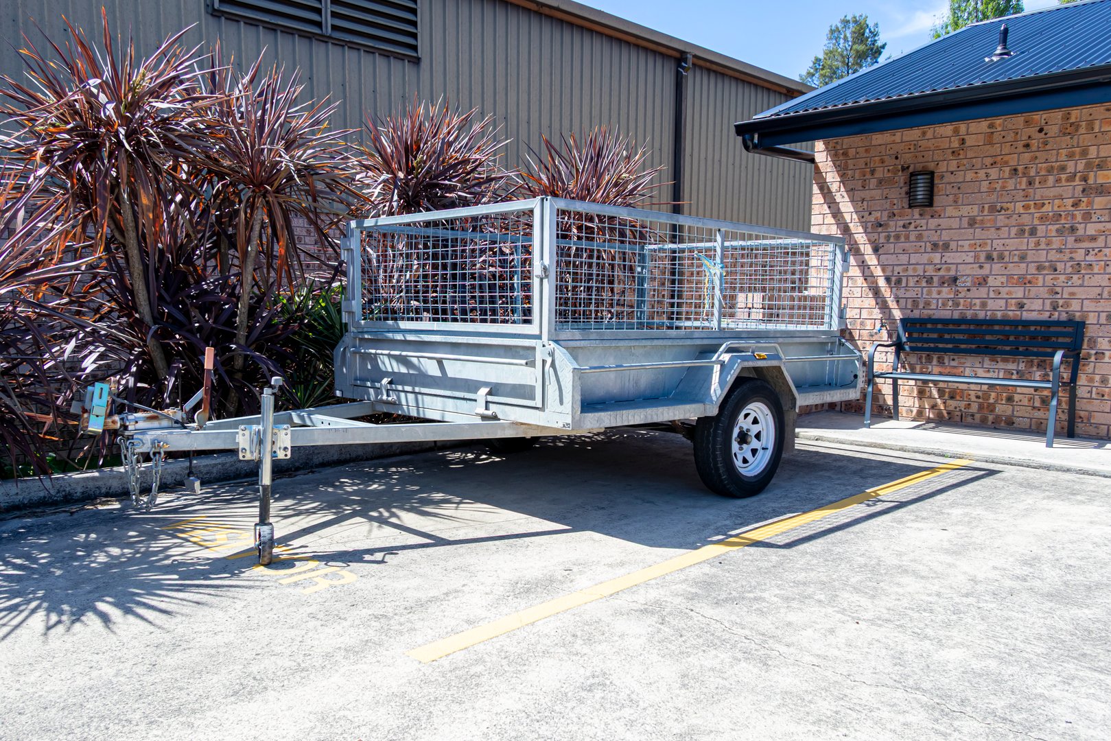 Photograph of a parked galvanized single axel steel trailer with a mesh cage section for securely holding various types of items while being transported.