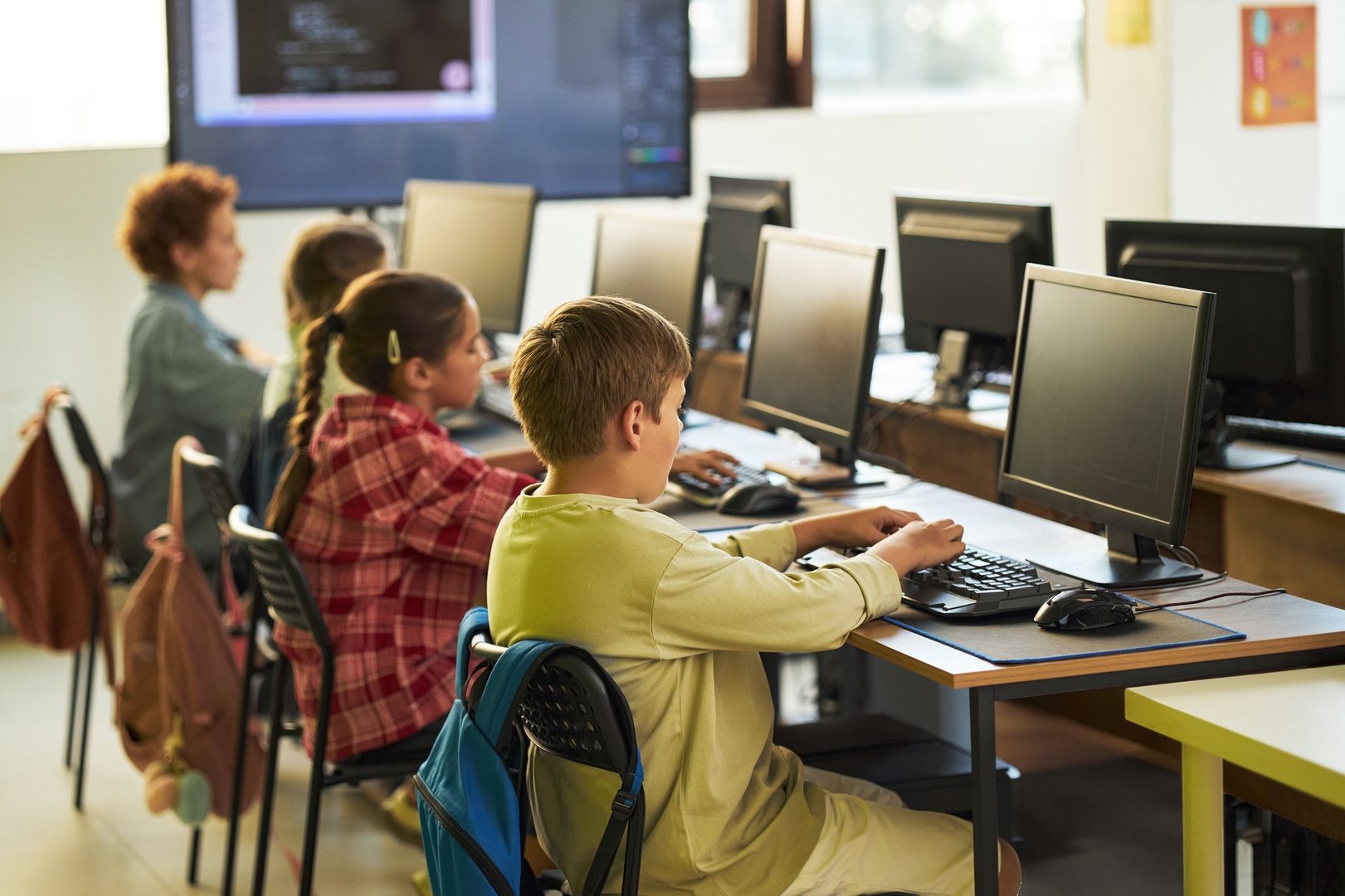Group of Caucasian and Hispanic children sitting at desks using desktop computers in classroom, focusing on typing and learning technology skills during school lesson