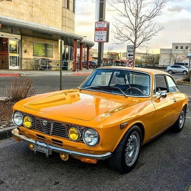 A classic yellow vintage car parked on a city street, featuring round headlights and distinctive grille design.