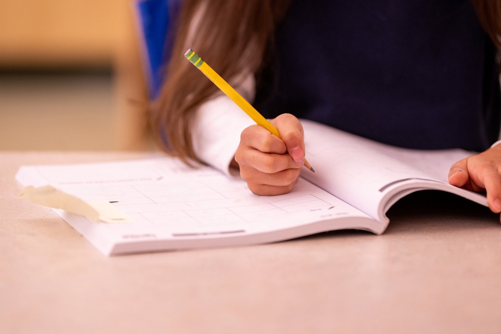 Close-up of student hand writing notes in open notebook, examination or textbook with number 2 pencil. Shows active learning and study process in educational setting.