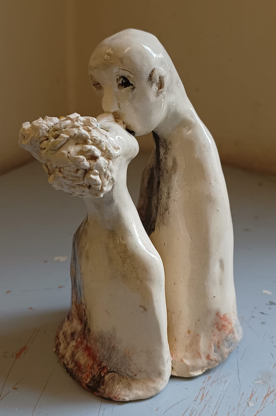 Abstract ceramic sculpture of two figures kissing, with textured surfaces and a simplistic design on a gray surface.