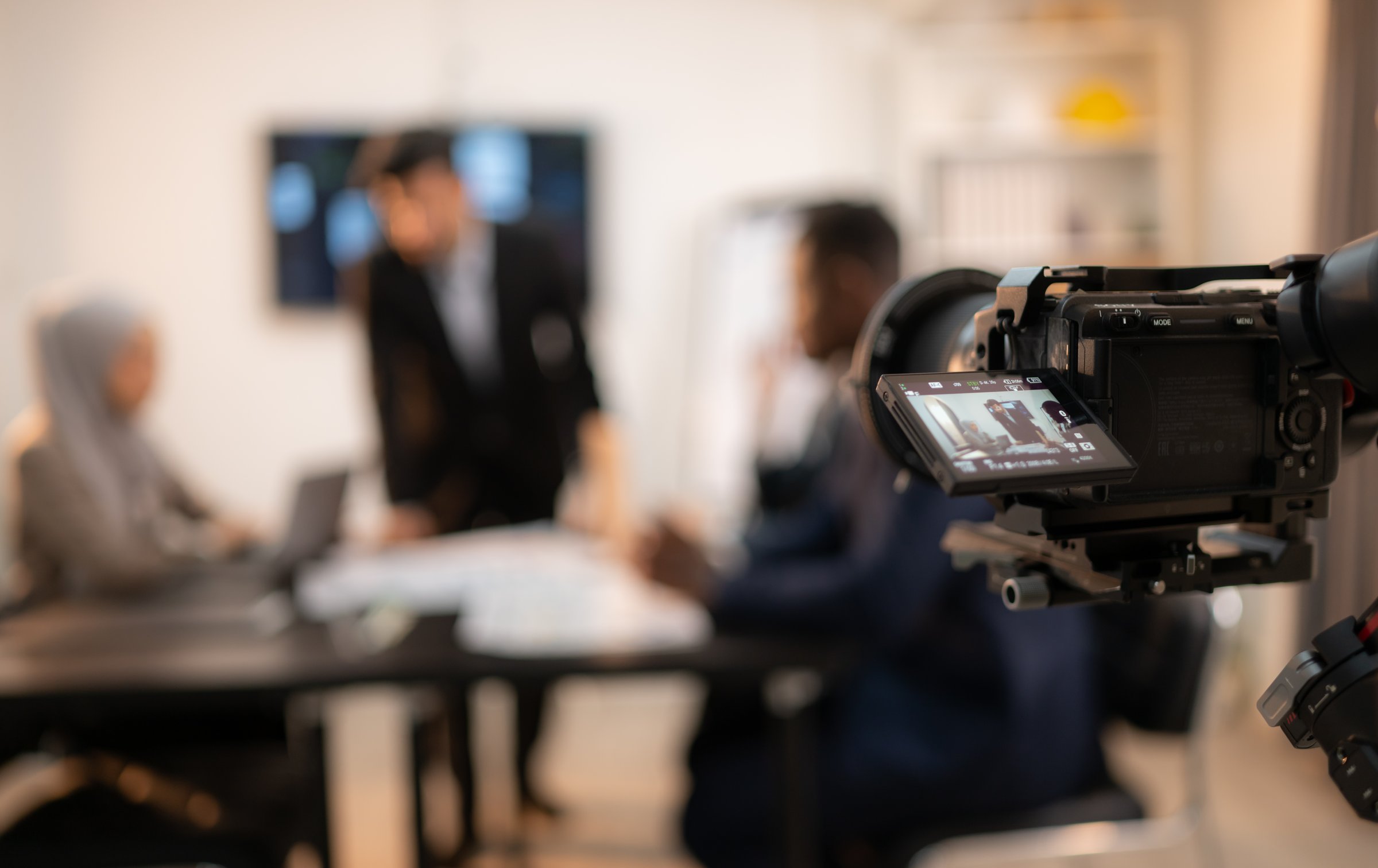 Blurred image of video camera on tripod and blurred business people working in background, Concept of shooting video company profile