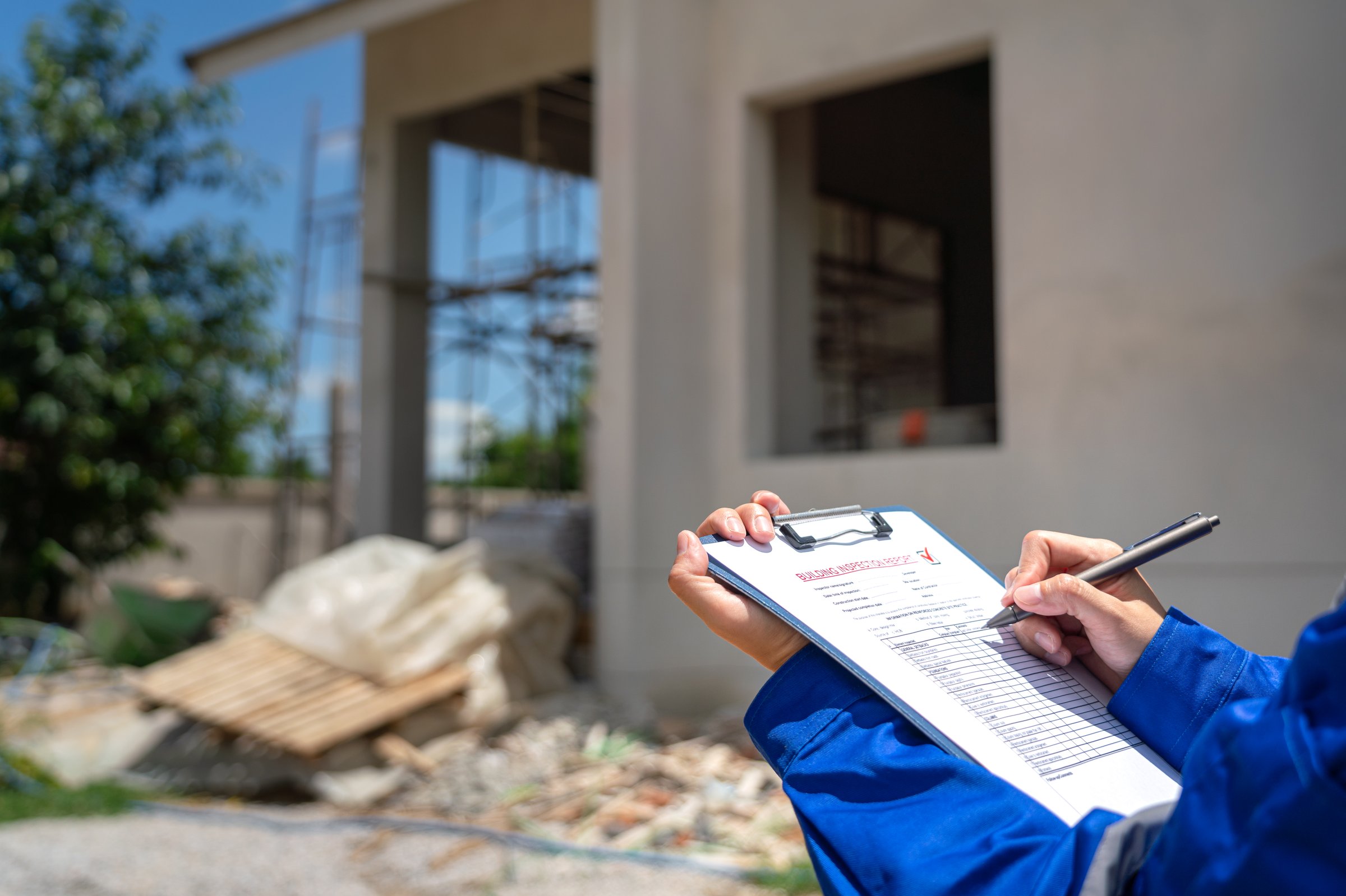 An architect is checking on house building quality checklist form to inspecting the progress with building house as blurred background. Construction industrial working scene, close-up.