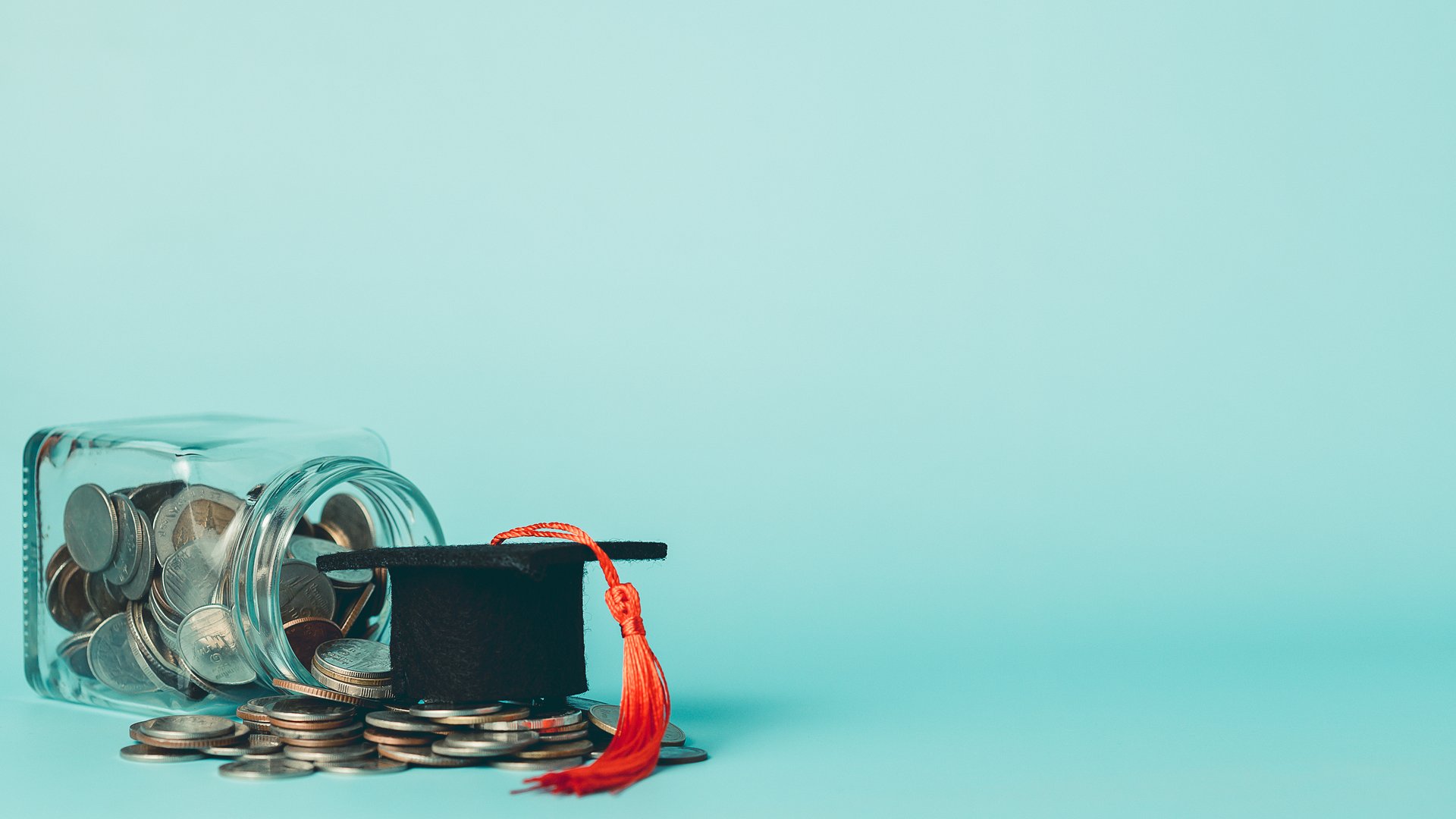 Coins in a glass jar with graduation cap on blue background. Concept of saving for education, student loans, scholarship, tuition fees, and financial planning.