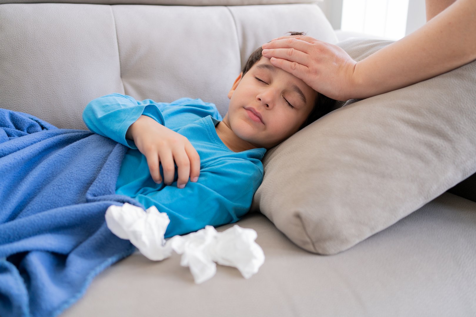 Flu, fever and mother with sick boy for health, virus or infection symptoms in bedroom. Family, childcare and hand of parent with child at home in couch to check temperature for cold, illness and flu