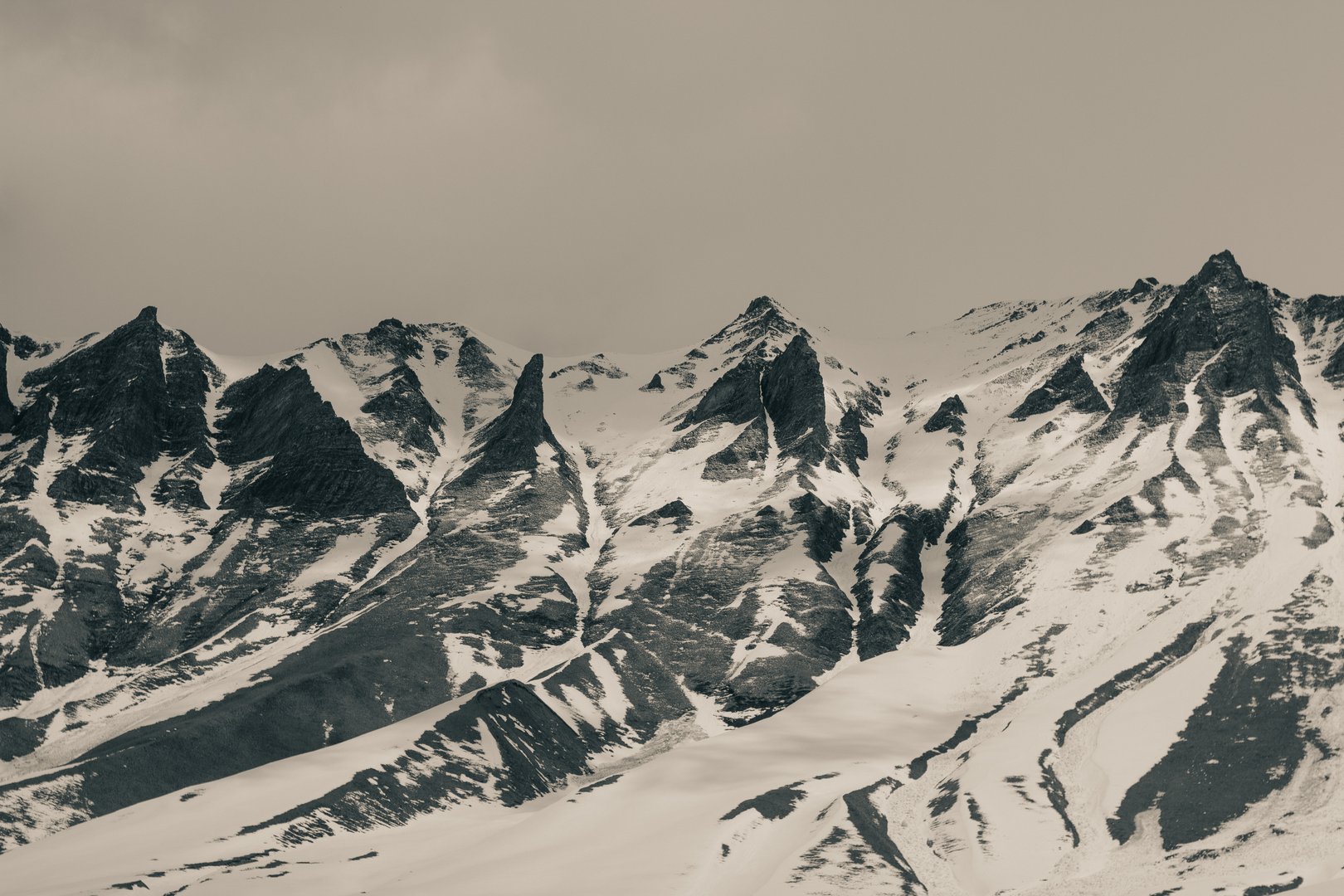 A powerful monochrome capture of the jagged Caucasus peaks in winter, where snow clings to steep cliffs and dramatic ridges slice through the sky