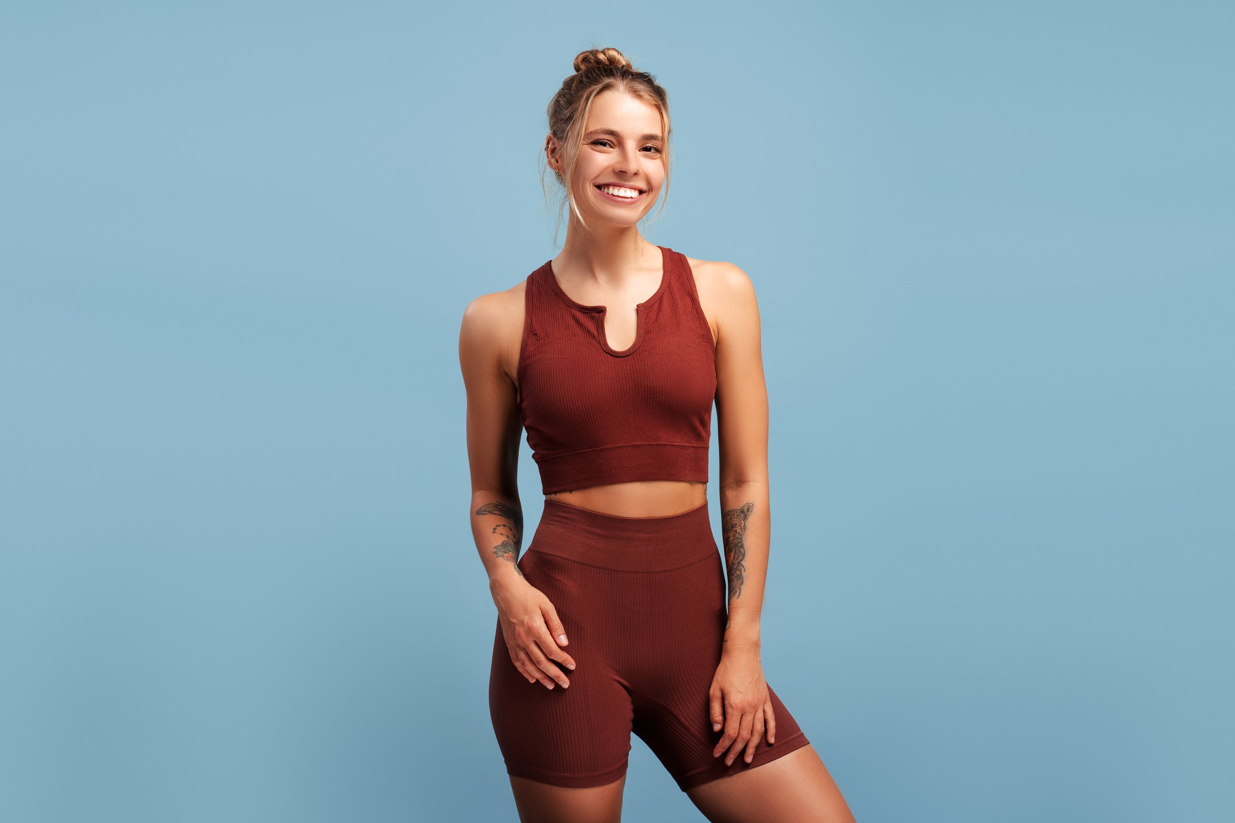 Positive sporty beautiful woman in sportwear looking at camera, isolated on blue background in studio. Sport, health care, wellness concept