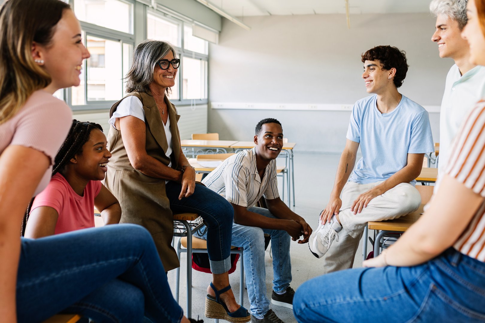 Young group of high school students talking with mature teacher in classroom. Education concept