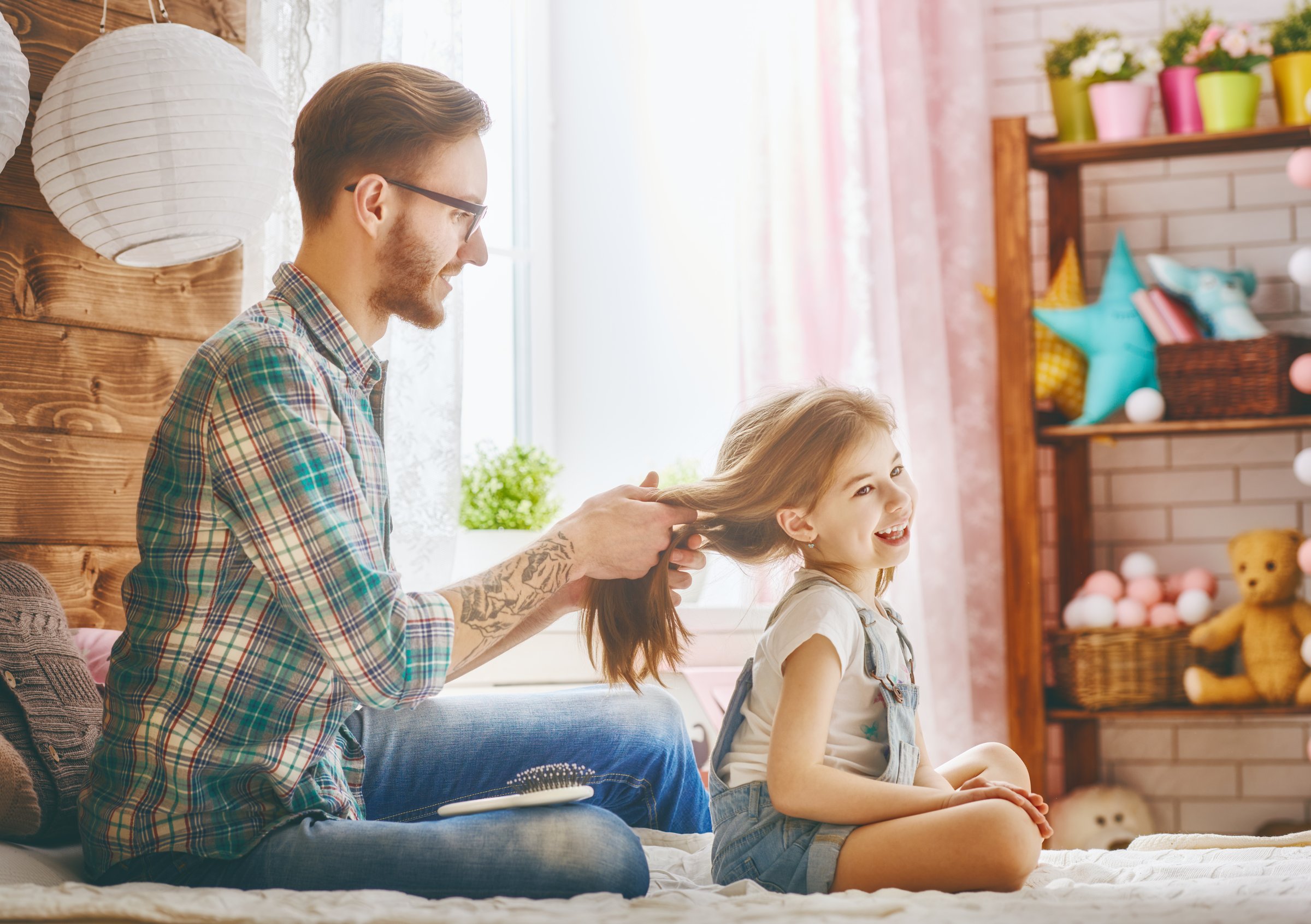 Happy loving family. Father is combing her daughter's hair sitting on the bed in the room.